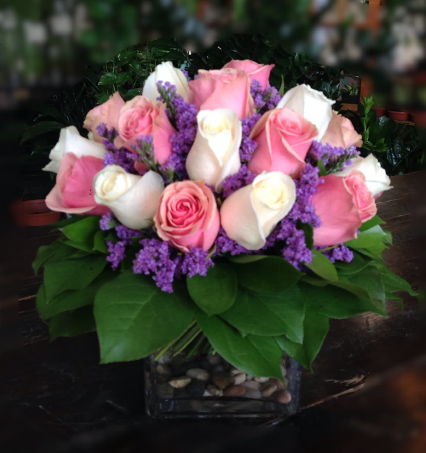 Pink and white roses arranged in a square glass vase with purple filler