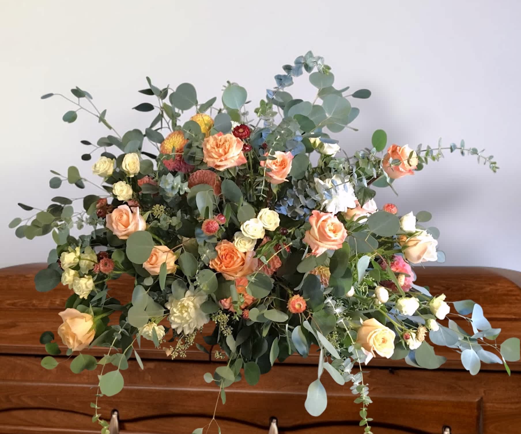 Low floral arrangement with peach roses and mixed greenery on a wooden surface
