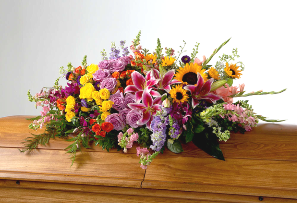 Colorful floral spray with lilies, roses, and sunflowers on a wooden casket