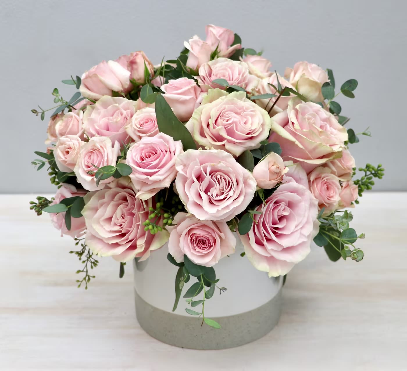 Pink roses arranged in a round white vase with eucalyptus