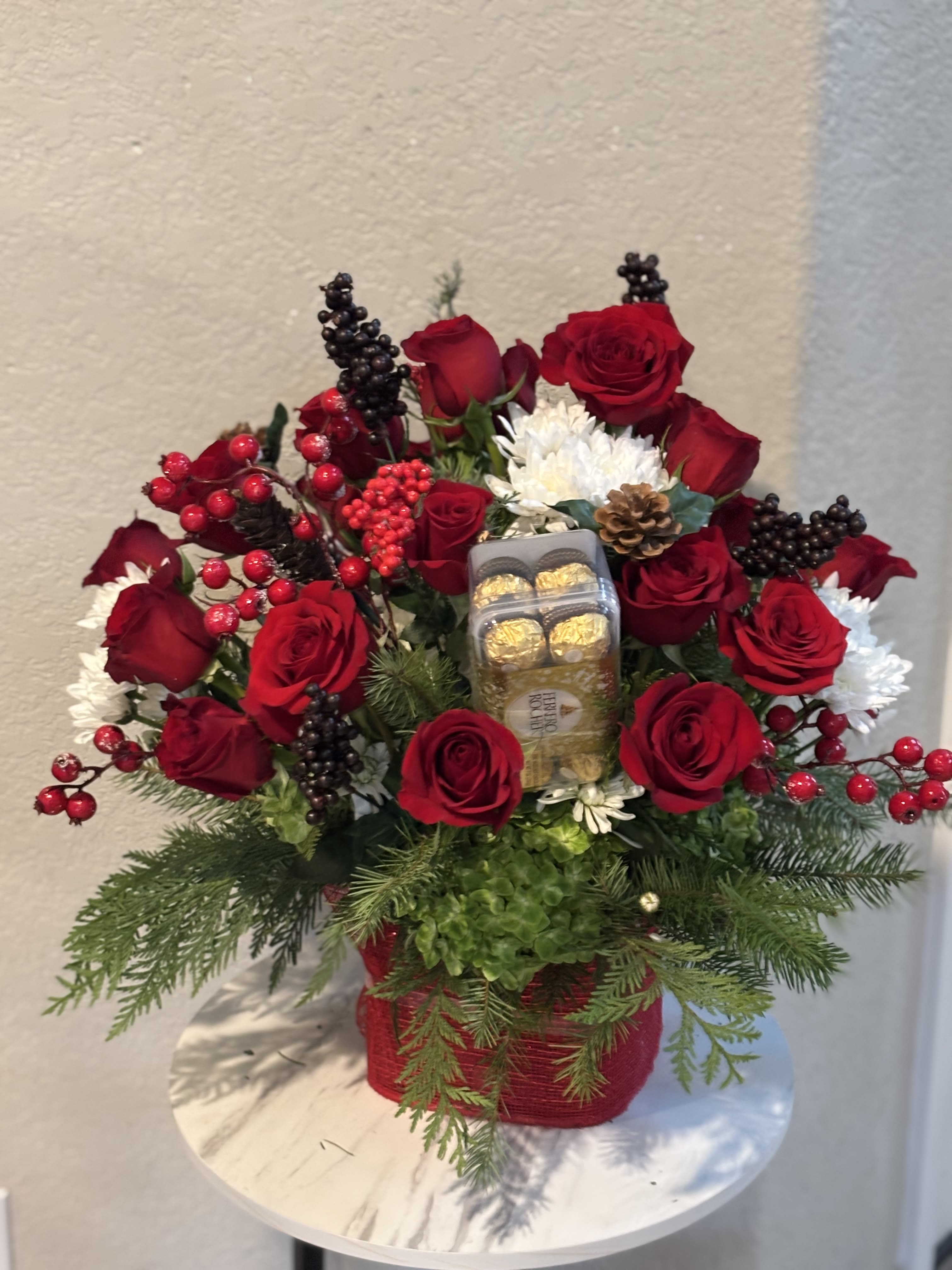 Romance | Premium Red Roses &amp; Ferrero Rocher - Celebrate the magic of the holidays with our Holiday Romance | Premium Red Roses &amp; Ferrero Rocher Christmas Arrangement, an elegant floral gift exclusively handcrafted by Snyder Flowers. This luxurious arrangement features premium long-stem red roses, Ferrero Rocher chocolates, fresh Christmas evergreens, hydrangea, white chrysanthemums, seasonal berries, pinecones and premium holiday greenery, beautifully designed in a festive keepsake container.  Perfect for Christmas celebrations, holiday gifts, anniversaries, romantic surprises, corporate gifts, hostess gifts, family gatherings and winter birthdays, this arrangement combines timeless red roses with gourmet chocolates to create an unforgettable gift. Every design is handcrafted using fresh premium flowers selected for exceptional beauty and long-lasting freshness.  Snyder Flowers proudly offers same-day flower delivery in San Antonio, serving Stone Oak, Alamo Heights, The Dominion, Shavano Park, Castle Hills, Medical Center, Helotes, Leon Valley, Schertz, Cibolo, Live Oak, Universal City, Boerne, Bulverde, Timberwood Park and surrounding communities.  Whether you're searching for Christmas flowers, red roses, holiday flower arrangements, Ferrero Rocher gift baskets, romantic flowers, luxury floral gifts, flower delivery in San Antonio or a trusted local florist, Snyder Flowers creates premium floral designs that make every holiday celebration unforgettable.