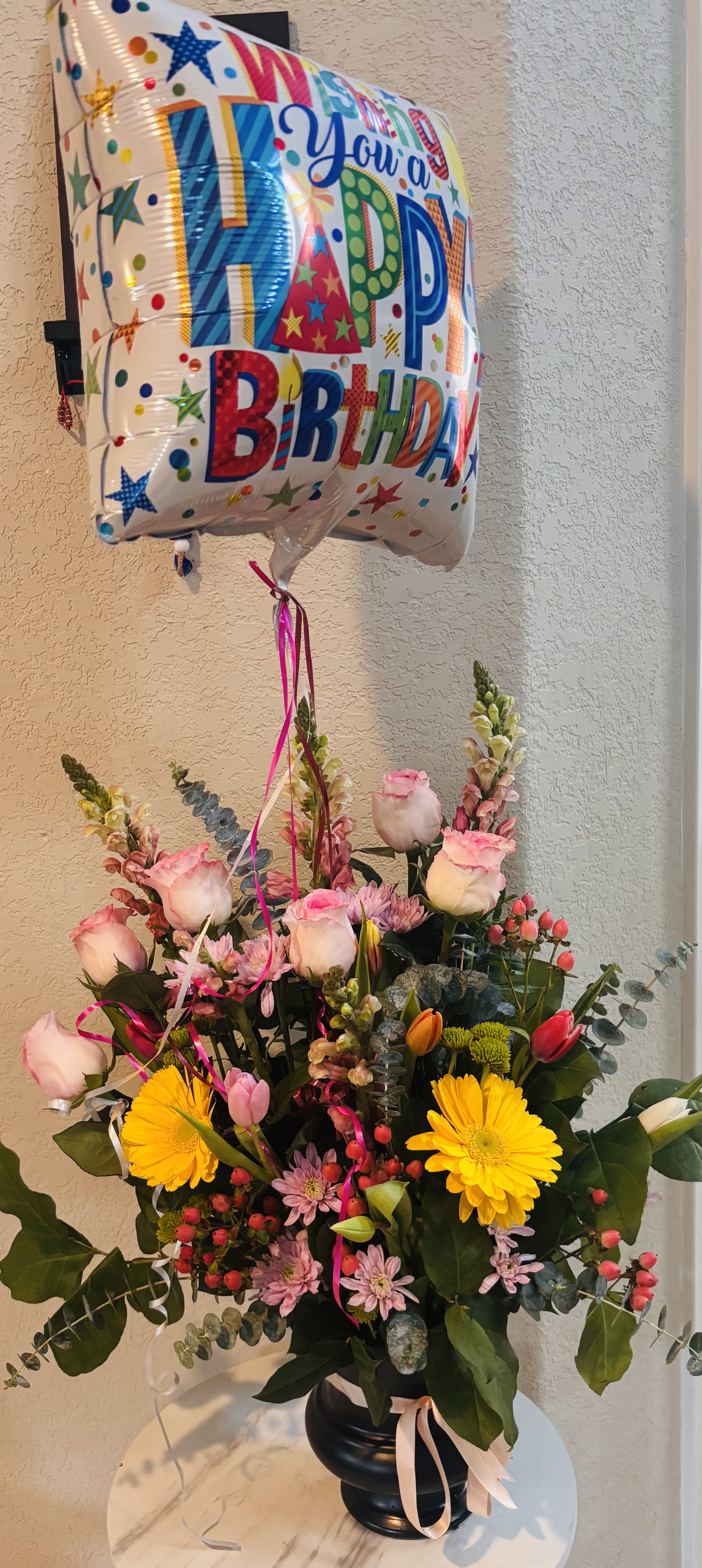 Happy Birthday Luxury Flower Arrangement with Balloon - A vibrant birthday flower arrangement in San Antonio featuring fresh pink roses, yellow gerbera daisies, tulips, snapdragons, chrysanthemums, hypericum berries, eucalyptus, and seasonal greenery, beautifully designed in an elegant container and paired with a festive birthday balloon. Handcrafted by Snyder Flowers San Antonio, this colorful floral gift is perfect to celebrate birthdays and create unforgettable moments.   A complete birthday gift with flowers and balloon that adds joy, color, and excitement to any celebration.  We proudly offer same-day flower delivery in San Antonio with fresh premium flowers and exceptional customer service.  Luxury floral designs created with high-quality blooms, vibrant colors, and modern elegant style.  Serving Stone Oak, Medical Center, Alamo Heights, Cibolo, Universal City, Live Oak, Helotes, Castle Hills, Shavano Park, and Downtown San Antonio.  Looking for a trusted florist in San Antonio, same day birthday flower delivery, or flowers with balloon near you? Snyder Flowers creates beautiful handcrafted floral gifts designed to impress and delivered fresh the same day.