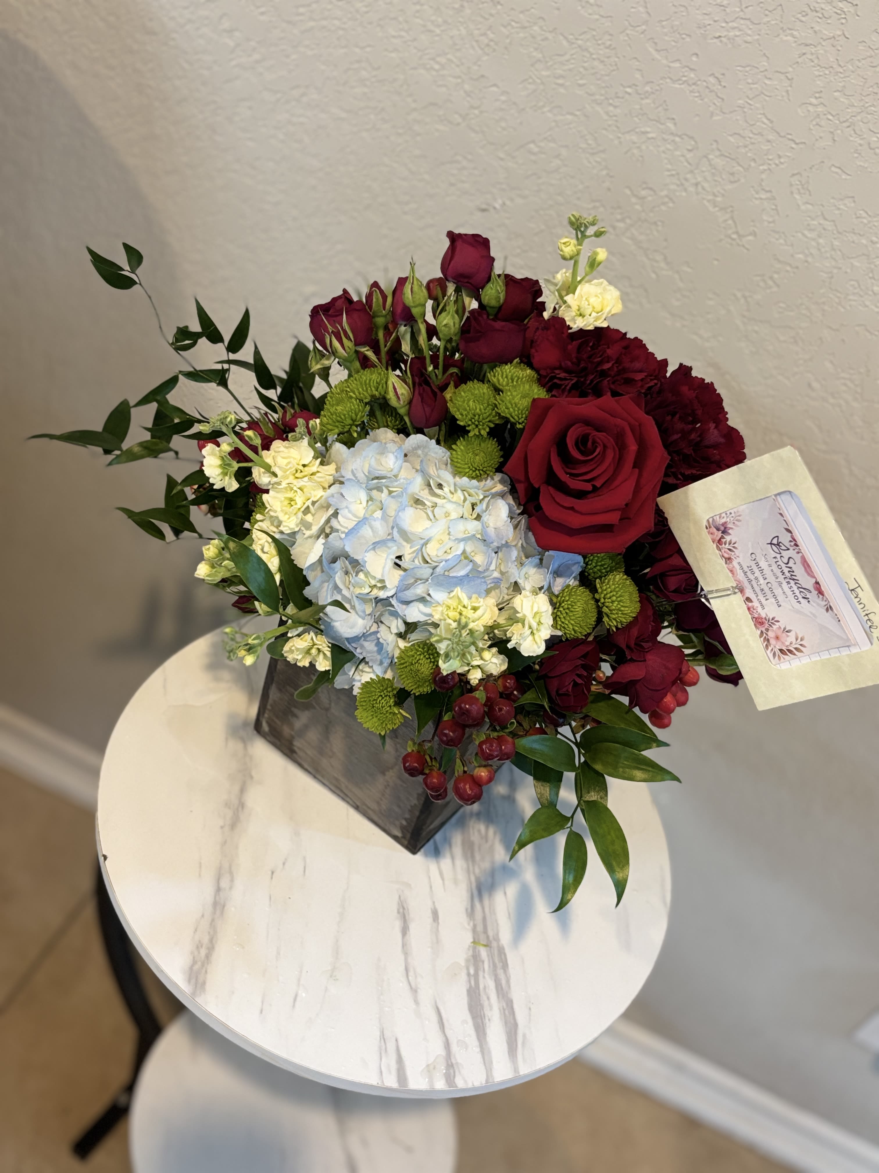 Crimson Elegance | Luxury Red Roses &amp; Blue Hydrangea Arrangement - Celebrate life's most meaningful moments with our Crimson Elegance | Luxury Red Roses &amp; Blue Hydrangea Arrangement, an exclusive floral design handcrafted by Snyder Flowers. This premium arrangement showcases luxurious long-stem red roses, delicate spray roses, a lush blue hydrangea, rich burgundy carnations, white stock flowers, green button chrysanthemums and vibrant hypericum berries, all arranged in a modern keepsake container with fresh seasonal greenery.  The timeless combination of red roses and hydrangeas creates an elegant gift for anniversaries, birthdays, romantic surprises, Valentine's Day, congratulations, thank you gifts, Mother's Day, housewarming celebrations and special occasions. Whether you're expressing love, appreciation or celebrating an important milestone, this arrangement delivers lasting beauty and sophistication.  We proudly offer same-day flower delivery in San Antonio, including Stone Oak, Alamo Heights, The Dominion, Shavano Park, Castle Hills, Medical Center, Helotes, Leon Valley, Schertz, Cibolo, Live Oak, Universal City, Boerne and surrounding communities.  If you're searching for red roses, hydrangea arrangements, luxury flowers, anniversary flowers, birthday flowers or flower delivery in San Antonio, trust Snyder Flowers to create unforgettable floral gifts with premium-quality blooms and exceptional service.