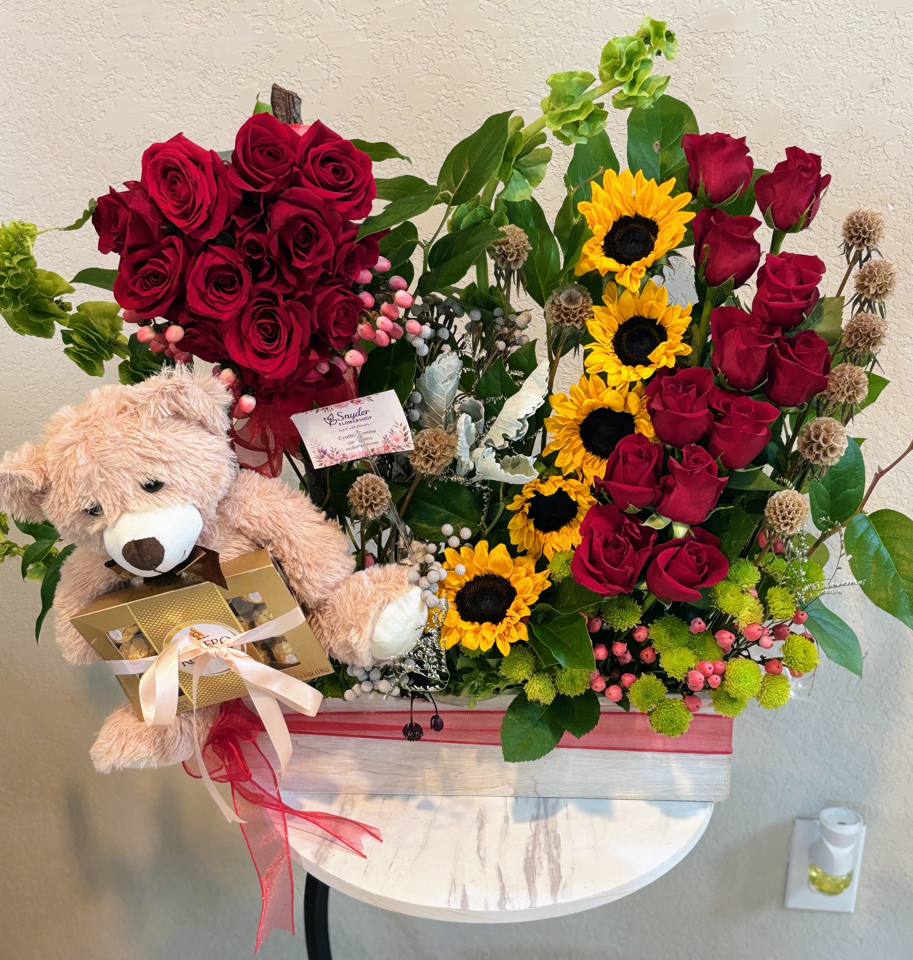 Ultimate Romance Gift Basket | Red Roses, Sunflowers, Teddy Bear &amp; Ferrero Rocher - Celebrate love with our Ultimate Romance Gift Basket, one of the most luxurious floral gifts created by Snyder Flowers. This premium design combines long-stem red roses, vibrant sunflowers, Ferrero Rocher chocolates, a soft teddy bear, hypericum berries, green button chrysanthemums and seasonal greenery in an elegant keepsake wooden box.  Designed for unforgettable moments, this arrangement is perfect for Valentine's Day, anniversaries, birthdays, romantic surprises, marriage proposals, congratulations, Mother's Day, date nights, celebrations and luxury gift giving. The combination of premium flowers, gourmet chocolates and a plush teddy bear creates a thoughtful gift that leaves a lasting impression.  Every arrangement is handcrafted using fresh premium flowers and is available with same-day flower delivery in San Antonio, including Stone Oak, Alamo Heights, The Dominion, Shavano Park, Castle Hills, Medical Center, Helotes, Leon Valley, Schertz, Cibolo, Live Oak, Universal City, Boerne and nearby communities.  If you're searching for red roses, sunflower arrangements, luxury flower gift baskets, Ferrero Rocher gifts, teddy bear flower gifts or same-day flower delivery in San Antonio, Snyder Flowers offers premium floral designs with exceptional quality and personalized service.