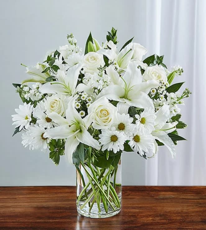White lilies, roses, and daisies arranged in a clear glass vase