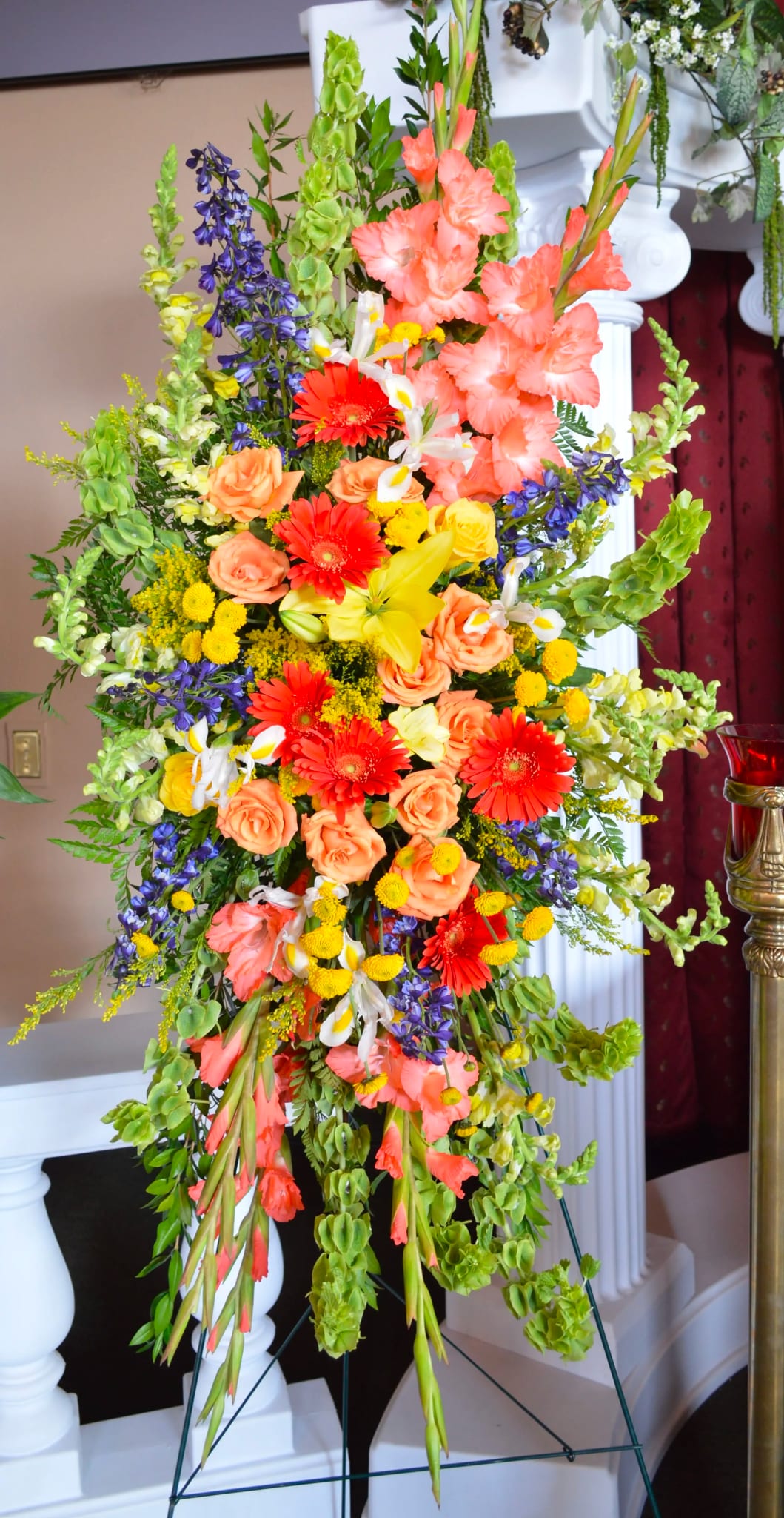 Tall floral standing spray with orange, yellow, purple, and white blooms