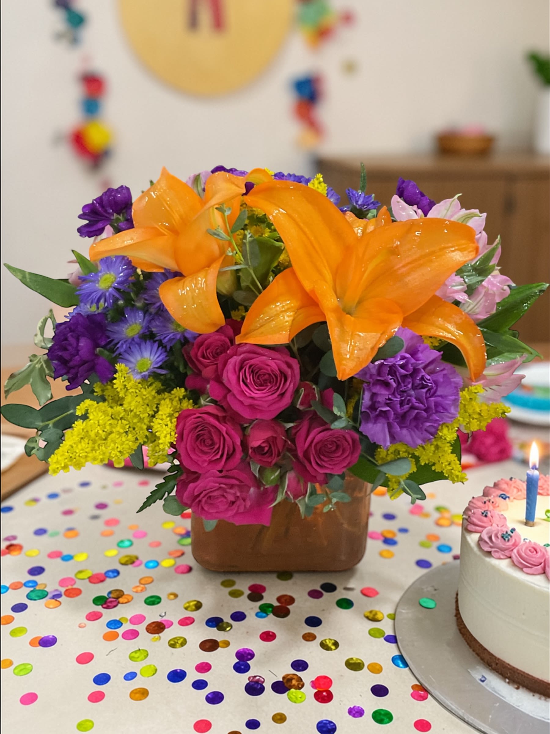 Color Pop - Color Pop is bright, bold, and built to stand out. A vibrant mix of orange lilies, hot pink roses, rich purple blooms, and cheerful yellow accents comes together in a design that feels energetic, balanced, and full of life.  The compact cube style keeps the look clean and modern, while the color palette does all the talking—playful, confident, and impossible to ignore without feeling chaotic.  Perfect for birthdays, celebrations, congratulations, thinking of you, or anytime you want to send something with a little extra personality and punch.  Each arrangement is designed with the freshest seasonal stems available. Colors and varieties may vary slightly to ensure the best overall look.  Available for local flower delivery through Aspen Tower Florist, serving Shelbyville and Greensburg along with Rushville, Batesville, Westport, Oldenburg, St. Paul, Waldron, and Milroy. 