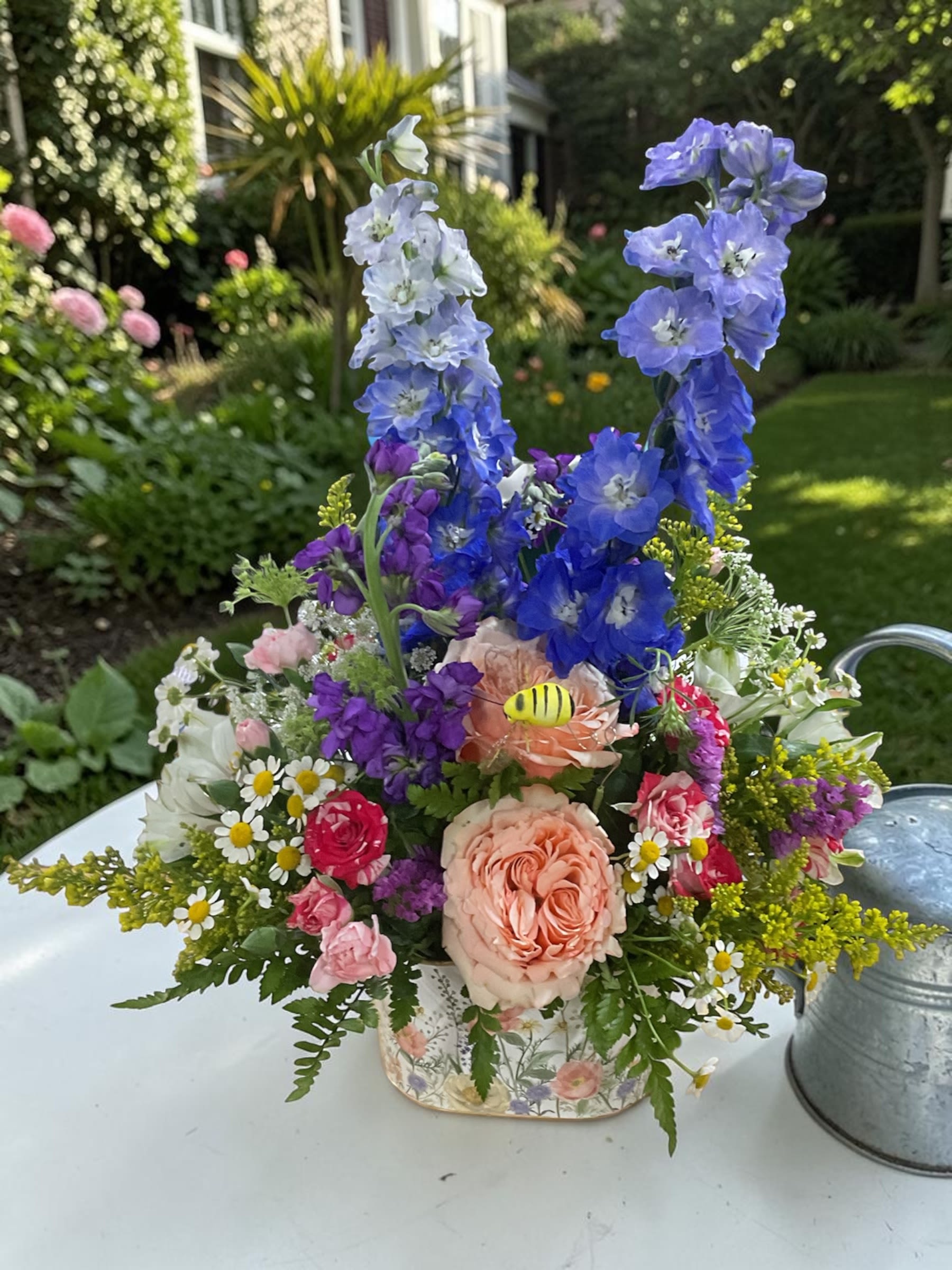 Fluttering Wildflowers - Celebrate with our charming Fluttering Wildflower garden arrangement from Aspen Tower Florist in Greensburg, Indiana. Available in Standard, Deluxe, and Premium sizes, this cheerful design is arranged in a keepsake floral container and features a fresh mix of roses, spray roses, delphinium, stock, alstroemeria, and seasonal accent flowers in soft spring colors. A cute little decorative bumblebee adds an extra touch of whimsy and sweetness.  Designed to feel fresh, airy, colorful, and full of movement, this arrangement is a beautiful gift for mothers, grandmothers, wives, daughters, and anyone you want to celebrate. Perfect for Mother’s Day, birthdays, thank you gifts, or just because.  Choose Standard for a thoughtful gesture, Deluxe for fuller impact, or Premium for a lush statement piece. Each arrangement is handcrafted and hand-delivered with care.  Flower varieties or colors may vary based on seasonal and supplier availability. If substitutions are needed, blooms of equal or greater value will be used while preserving the same overall style, color palette, and look of the arrangement.  Aspen Tower Florist proudly delivers in Greensburg, Batesville, Shelbyville, Rushville, North Vernon, Westport, Hope, and surrounding Indiana communities.