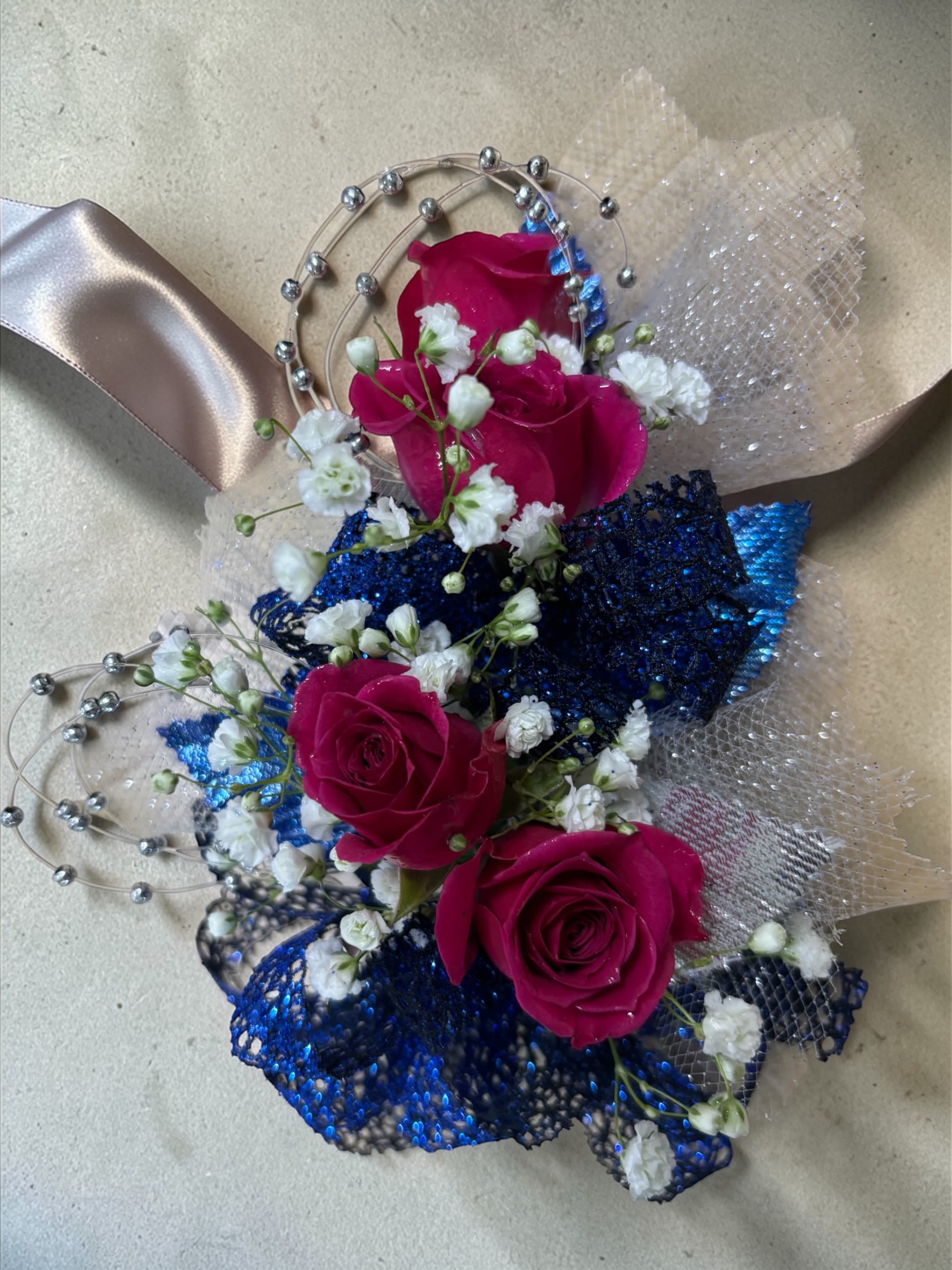 Fuchsia Nights Corsage Only - Fuchsia Nights – Corsage Only  Vibrant fuchsia roses, royal blue ribbon, silver accents, and delicate filler flowers come together in Fuchsia Nights, a bold wrist corsage collection designed for prom, homecoming, dances, banquets, weddings, and formal events. The striking combination of bright fuchsia and rich royal blue creates a dramatic look that stands out beautifully in photographs while maintaining elegant style.  Standard includes 3 spray roses. Deluxe includes 4 spray roses for added fullness and floral detail. Premium includes 5 spray roses for maximum flower coverage and visual impact.  Looking for the matching boutonniere? Find the complete Fuchsia Nights Corsage &amp; Boutonniere Set in our Prom category.  Because each corsage is individually designed, no two pieces will be exactly alike. Ribbon, filler flowers, bracelets, decorative accents, and other design elements may vary based on availability. While individual details may differ, the overall color palette, roses and/or flowers, style, and appearance of the Fuchsia Nights collection will be maintained.