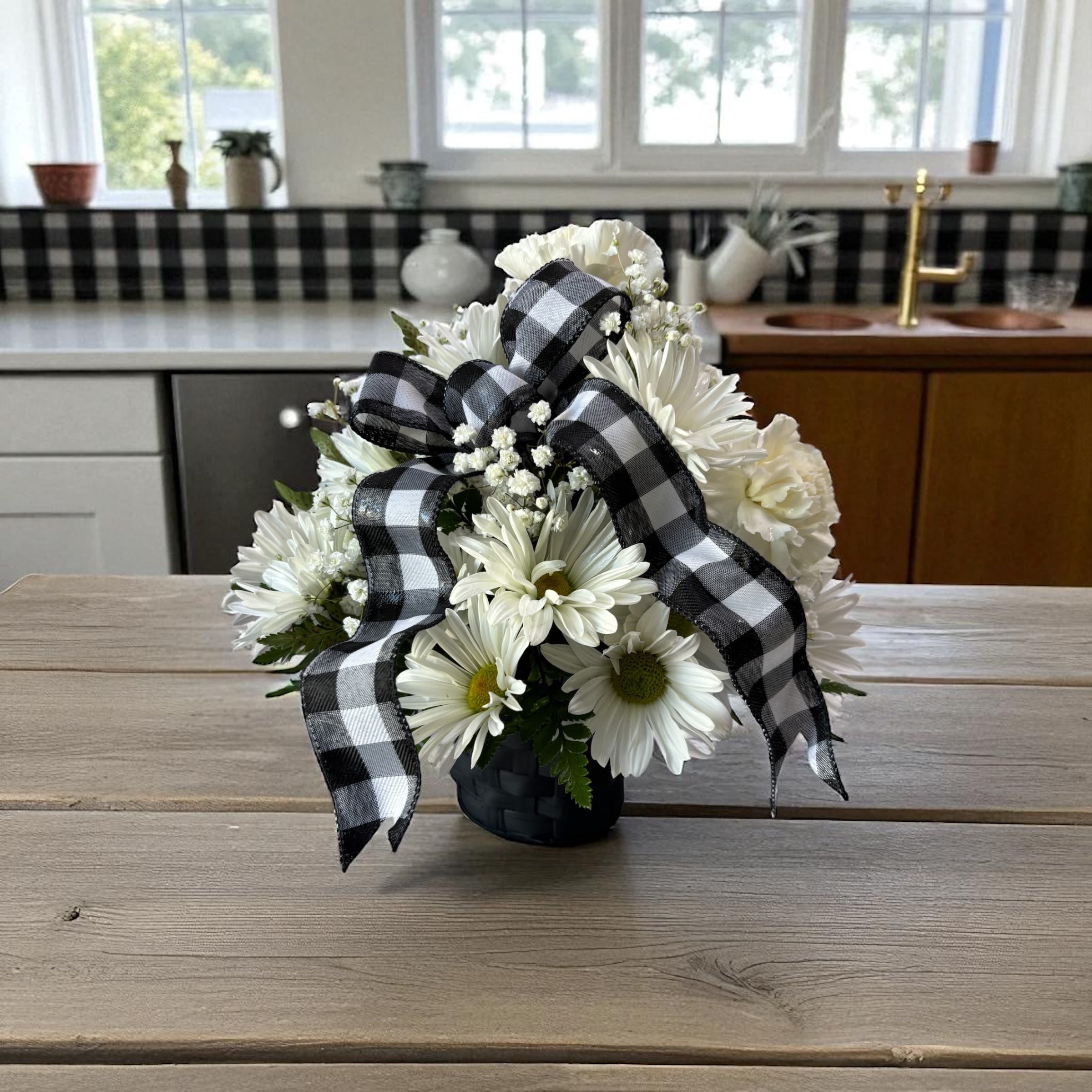 Farmhouse Fabulous - Bring rustic charm home with Farmhouse Fabulous, a fresh flower arrangement featuring white blooms, soft green accents, and classic black-and-white buffalo check ribbon. Perfect for birthdays, housewarmings, thank-you gifts, get well flowers, hostess gifts, new homes, farmhouse décor lovers, and everyday flower delivery.  Standard features white daisies and white carnations arranged in a black basket with buffalo check ribbon.  Deluxe includes green mini hydrangea, white daisies, white chrysanthemums, and white spray roses arranged in a glass 4-inch cube vase with buffalo check ribbon.  Premium includes green mini hydrangea, white daisies, white chrysanthemums, white roses, and white spray roses arranged in a glass 5-inch cube vase with buffalo check ribbon for added fullness and visual impact.  Each arrangement is handcrafted and may vary slightly based on flower availability. The overall color palette, farmhouse style, and appearance of Farmhouse Fabulous will be maintained.