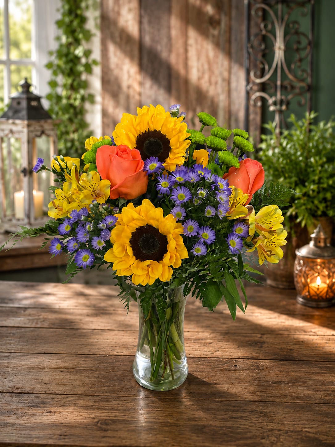 Painted Summer - Remember those perfect summer days when the sun was shining, the flowers were blooming, and life felt a little lighter? Painted Summer was inspired by that feeling.  Bursting with vibrant sunflowers, coral roses, purple asters, yellow alstroemeria, green button poms, and fresh seasonal greenery, this cheerful floral arrangement brings the warmth and beauty of a summer garden indoors. Bright, colorful, and full of life, it’s designed to create smiles and brighten ordinary days.  Perfect for birthdays, anniversaries, thank you gifts, get well wishes, congratulations, thinking of you moments, friendship gifts, and everyday celebrations, Painted Summer delivers more than flowers—it delivers happiness. Its joyful blend of colors creates an uplifting presence that instantly transforms a room and reminds someone they are loved, appreciated, and remembered.  The Standard version offers a beautiful expression of summer beauty. The Deluxe version includes additional blooms for greater fullness and impact. The Premium version features even more flowers, creating a lush garden-inspired presentation designed to impress from every angle.  Painted Summer is a bright reminder that sometimes the most meaningful gifts are the ones that make someone smile for no reason at all.