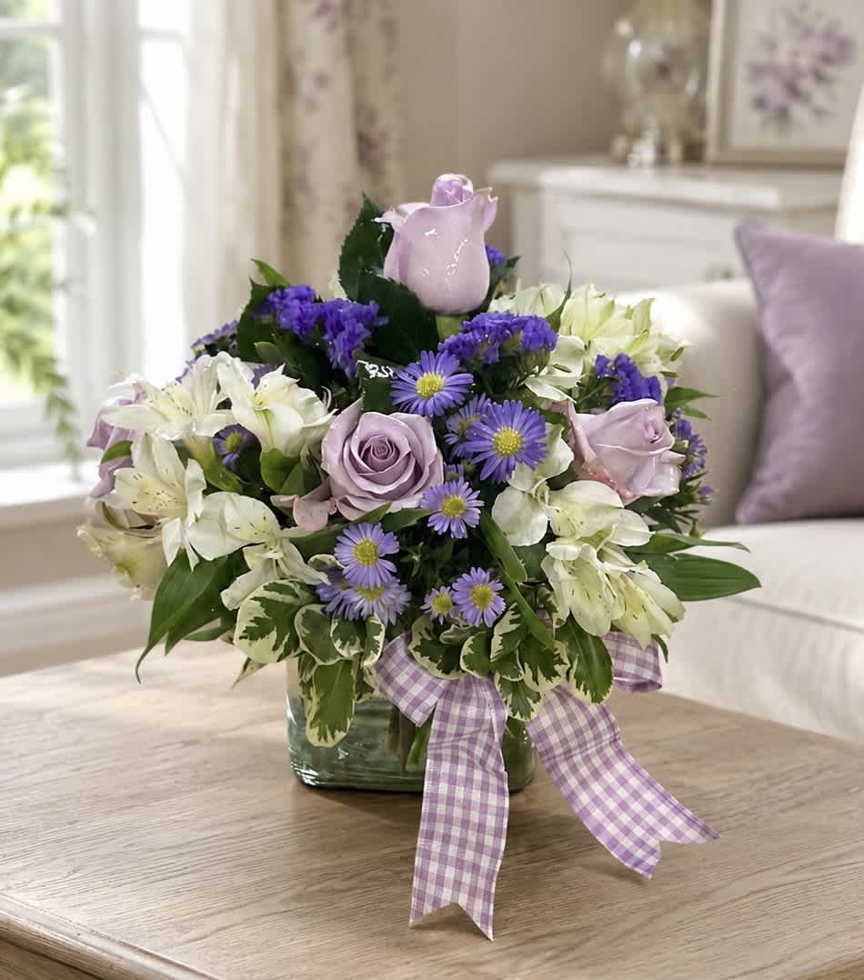 Lavender roses and white lilies in a glass vase with a purple ribbon