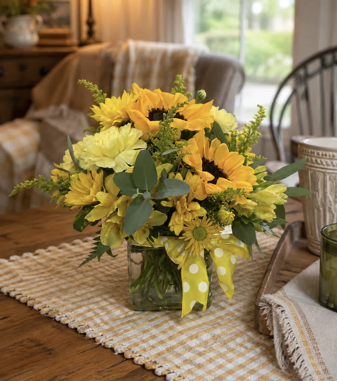 Yellow sunflower and daisy bouquet in a glass vase with a polka-dot ribbon