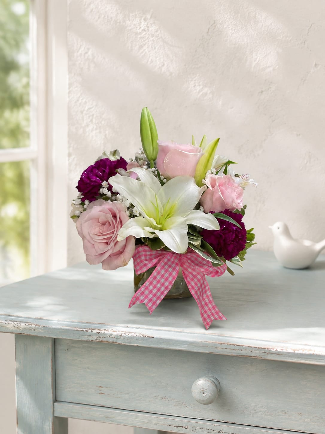Pink and white flower arrangement in a glass vase with a gingham ribbon