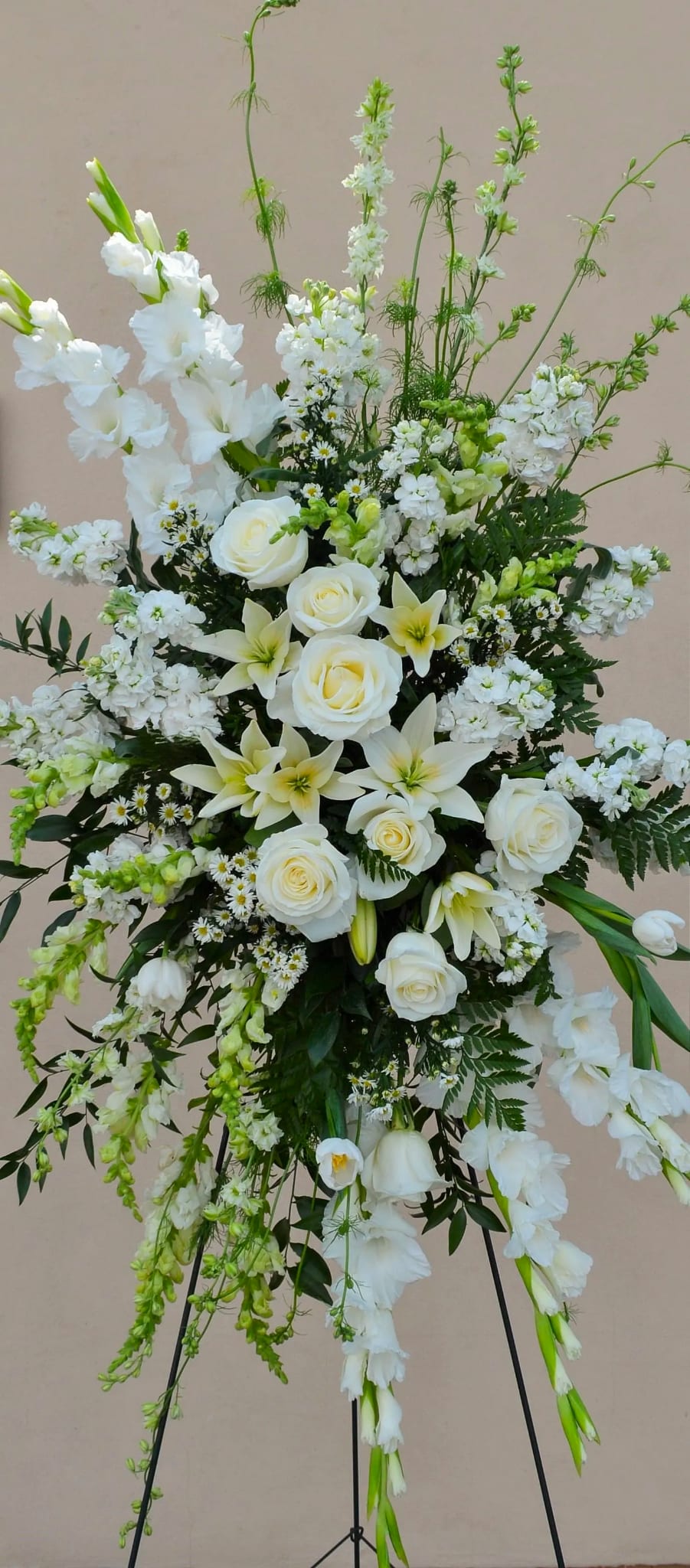 White floral standing spray with roses and lilies on a black easel