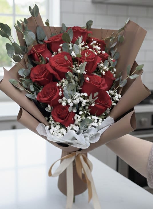 Bouquet of red roses with white filler flowers and eucalyptus in brown paper