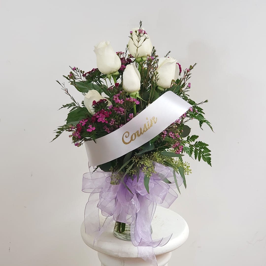 White roses in a glass vase with a lavender ribbon and sash