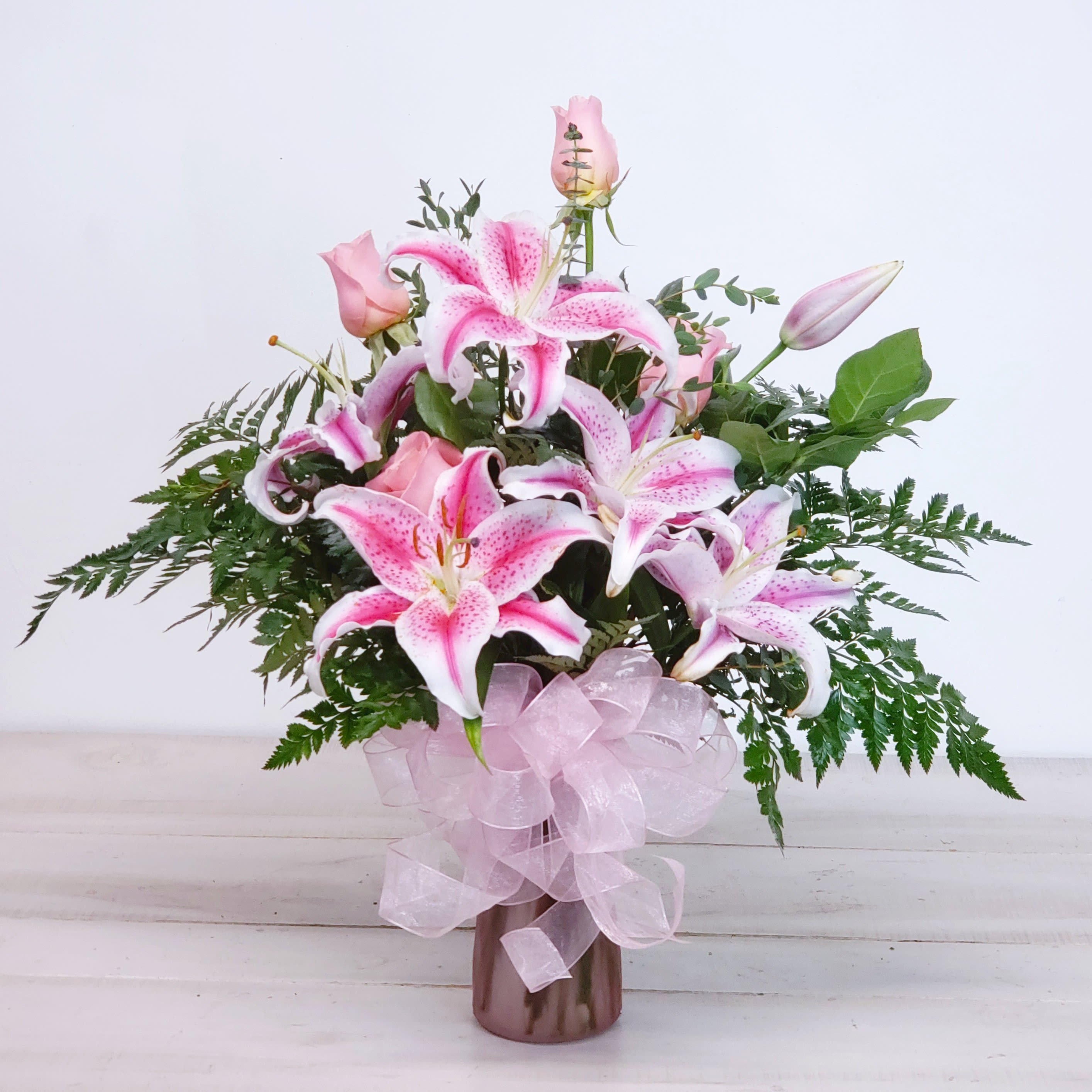 Pink lilies and roses in a vase with a pink ribbon bow
