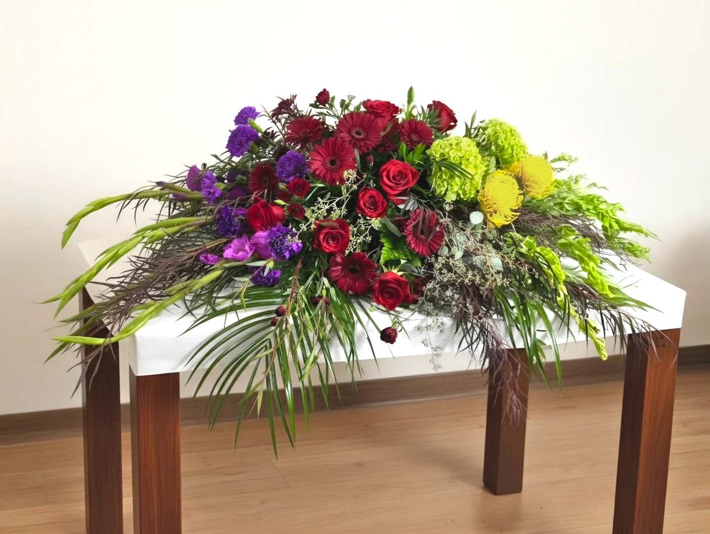 Long floral centerpiece with red, purple, and yellow blooms on a white table