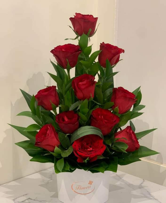 Red roses arranged in a white box with green leaves