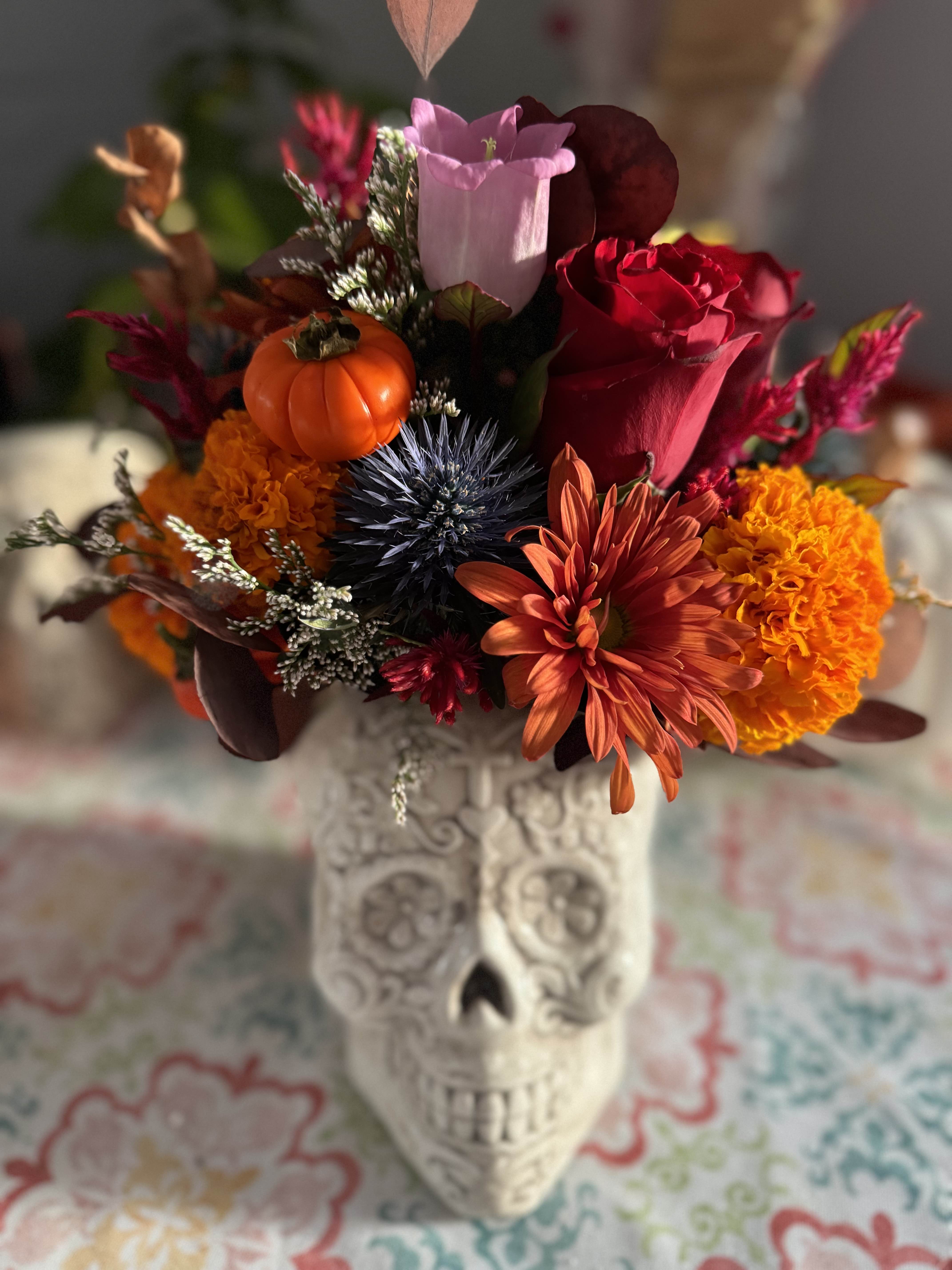 Autumn bouquet in a skull vase with roses, mums, and a small pumpkin