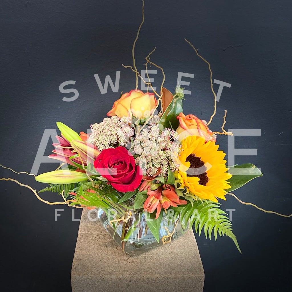 Mixed bouquet with roses, lilies, sunflowers, and alstroemeria in a glass vase
