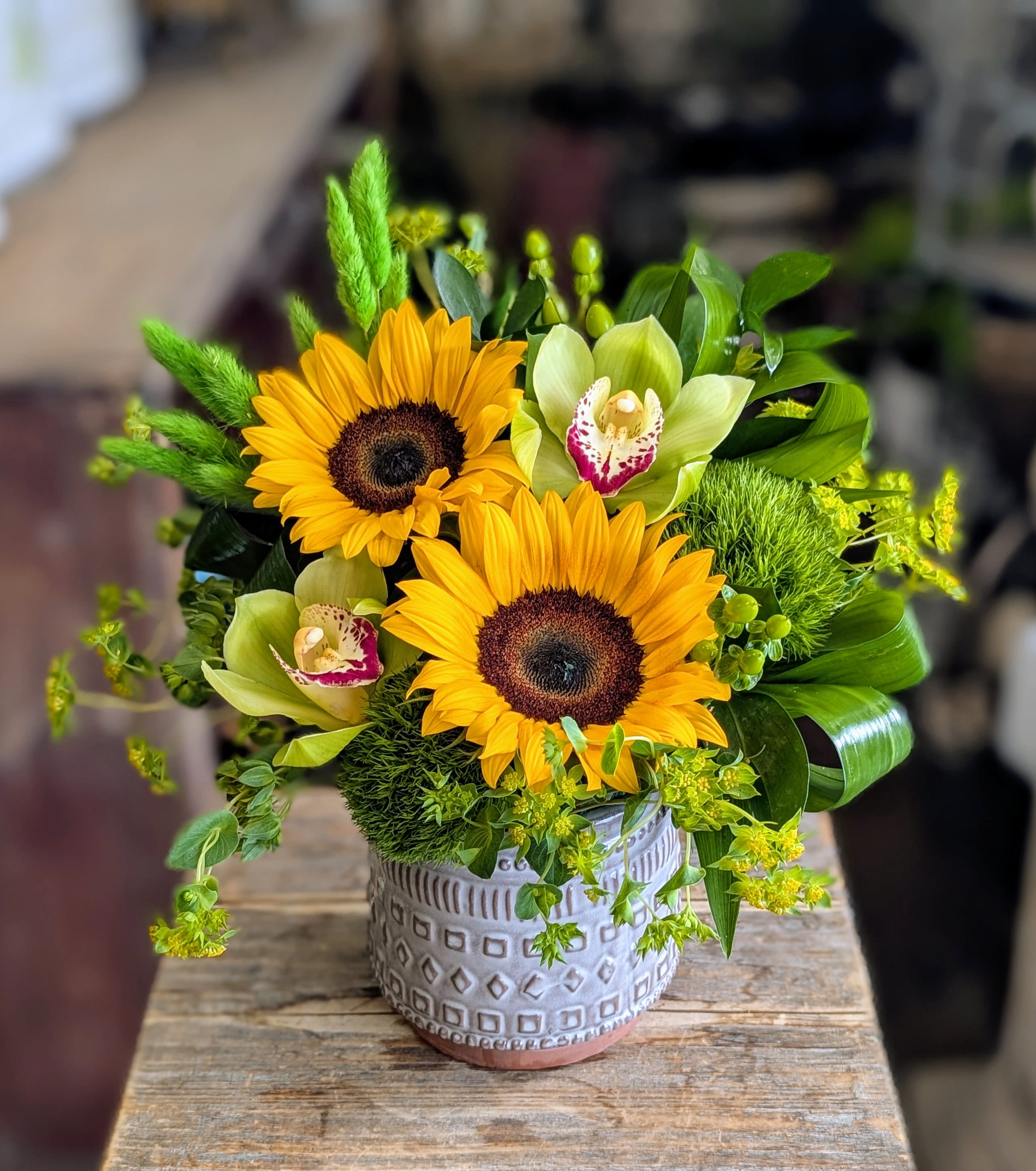 Sunny - Say hello to Sunny—a vibrant sunflower and orchid arrangement from Windmill Floral Expressions, your go‑to florist in Las Vegas and Henderson. This lively design features bold, golden sunflowers paired with striking green cymbidium orchids, lush seasonal greenery, and textured accents that create a fresh, modern look.  Hand‑crafted in a stylish ceramic container, Sunny is perfect as a cheerful birthday gift, a bright thank‑you bouquet, or a gorgeous centerpiece to elevate your home or office décor. Its radiant mix of blooms makes it a popular choice for same‑day flower delivery in Las Vegas and Henderson, spreading joy and natural beauty wherever it goes.  Bring the sunshine in—order Sunny today from Windmill Floral Expressions and let every petal brighten your day.  