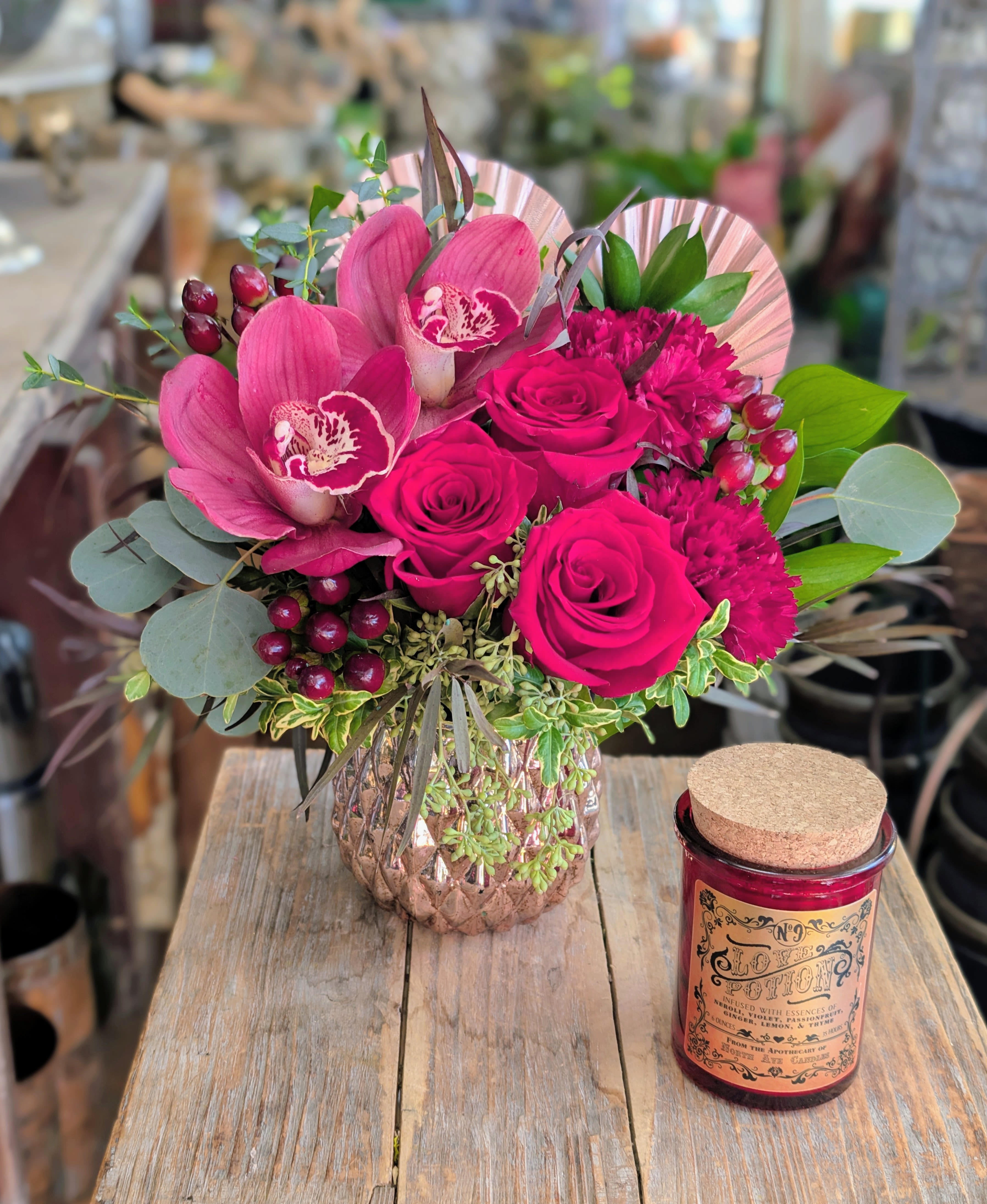 Pink roses and orchids in a glass vase beside a red candle jar