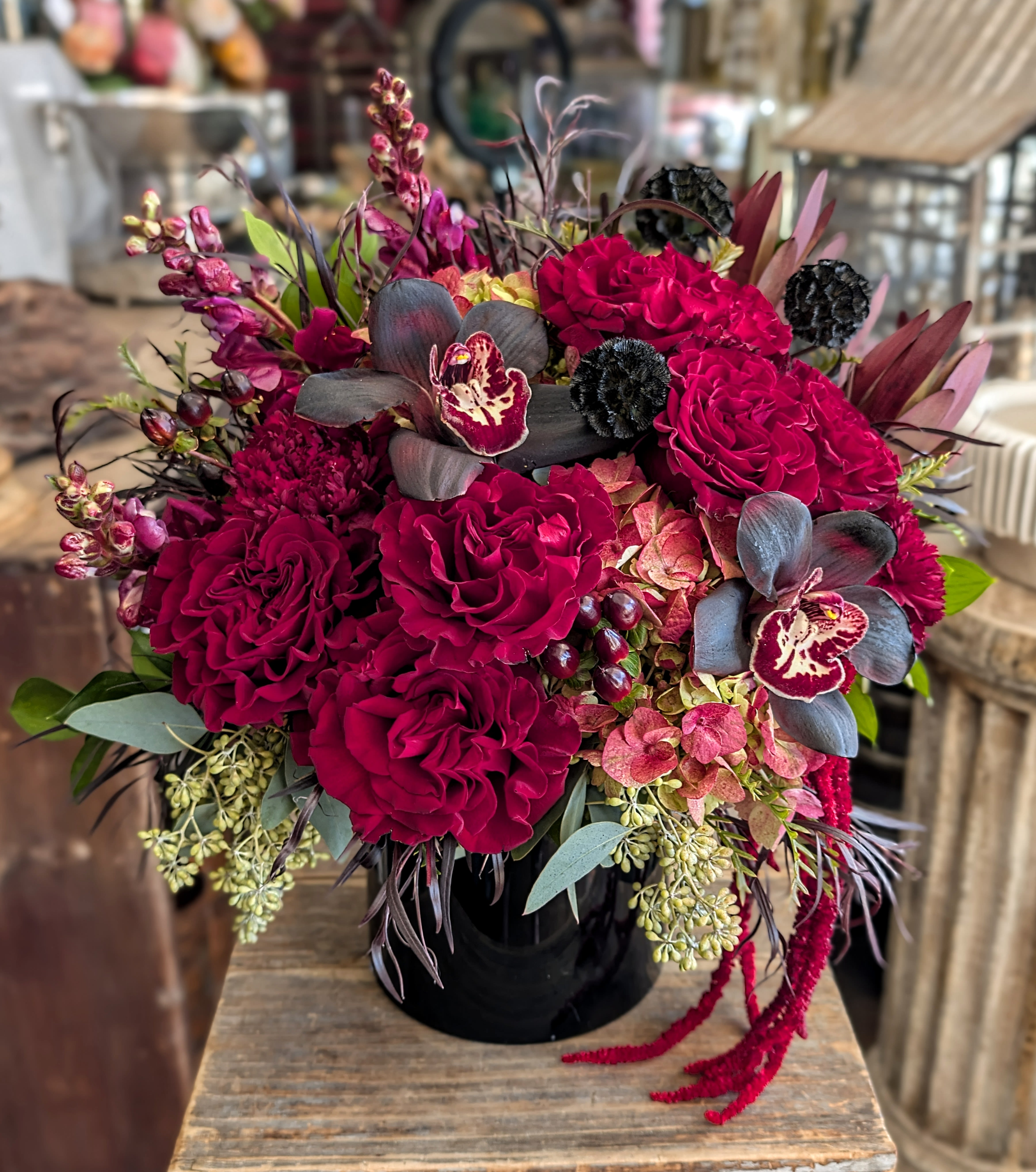 Nightfall - Nightfall is a dramatic expression of modern romance, where deep crimson garden roses meet inky cymbidium orchids, blush-toned hydrangea, and rich hypericum berries, all gathered into a sleek black vessel. Designed to feel both luxurious and mysterious, this arrangement captures the magic of twilight—bold, moody, and unforgettable.  Handcrafted by Windmill Floral Expressions, this petite yet powerful design blends velvety textures with layered botanical elements, creating a striking centerpiece for Valentine’s Day, anniversaries, birthdays, or meaningful moments that deserve something extraordinary. Subtle seasonal accents and curated greenery add movement and depth, making Nightfall a true statement piece.  Perfect for lovers of modern floral design and dark romance aesthetics, Nightfall is ideal for gifting or elevating your space with a touch of elegance and intrigue. Available for same-day flower delivery in Las Vegas and Henderson, including Anthem, Inspirada, Ascaya, and MacDonald Ranch. As a local, family-owned florist, we specialize in custom floral arrangements and boutique designs crafted with care and artistry.  Let Nightfall set the mood—where passion meets petals, and every detail tells a story.