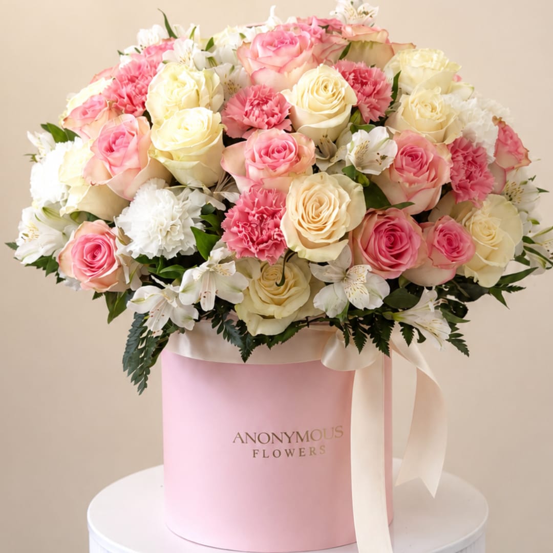 Pink and cream roses with white carnations in a pink hat box