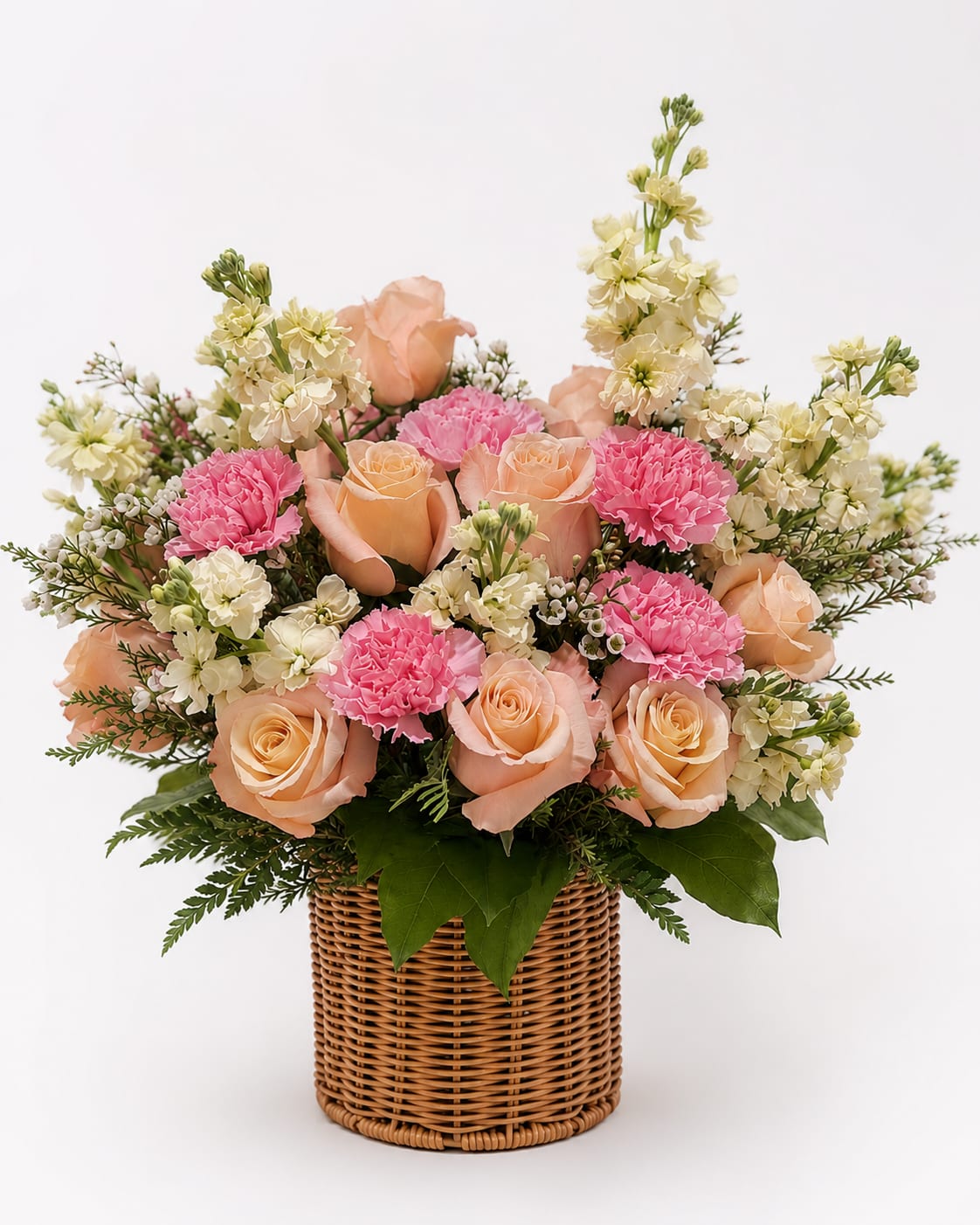 Peach Blossom Basket - A charming basket arrangement featuring elegant peach roses, soft pink carnations, creamy stock flowers, delicate waxflower, and lush greenery. Designed in a classic woven basket, this fresh and cheerful arrangement brings warmth and timeless beauty to bi
