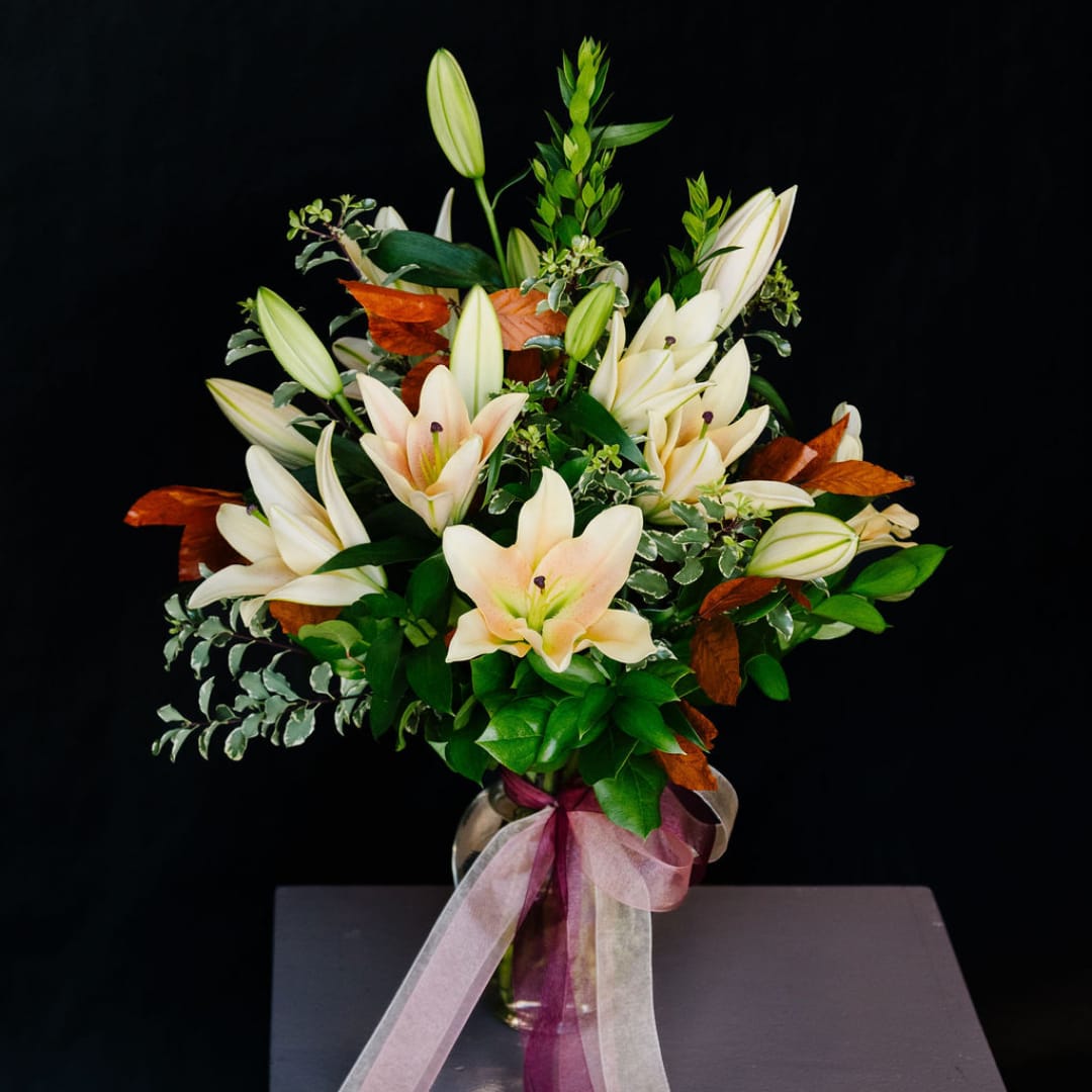 Bouquet of white lilies in a glass vase with a pink ribbon