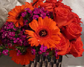 Orange gerbera daisies and red roses with purple filler flowers in a basket