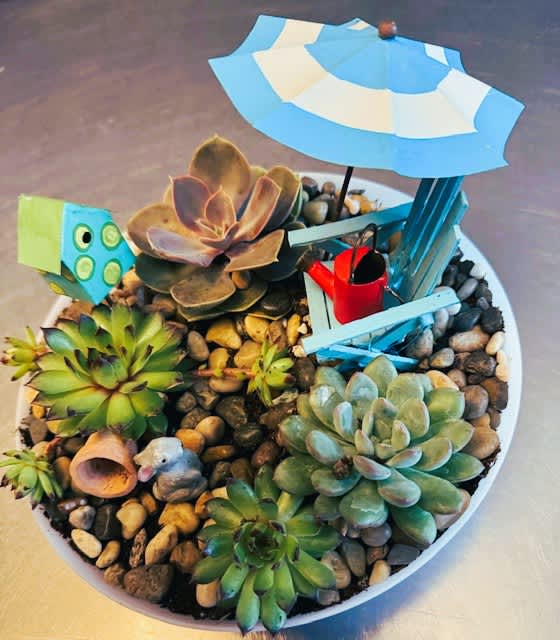 Succulent arrangement in a white bowl with a tiny beach chair and umbrella