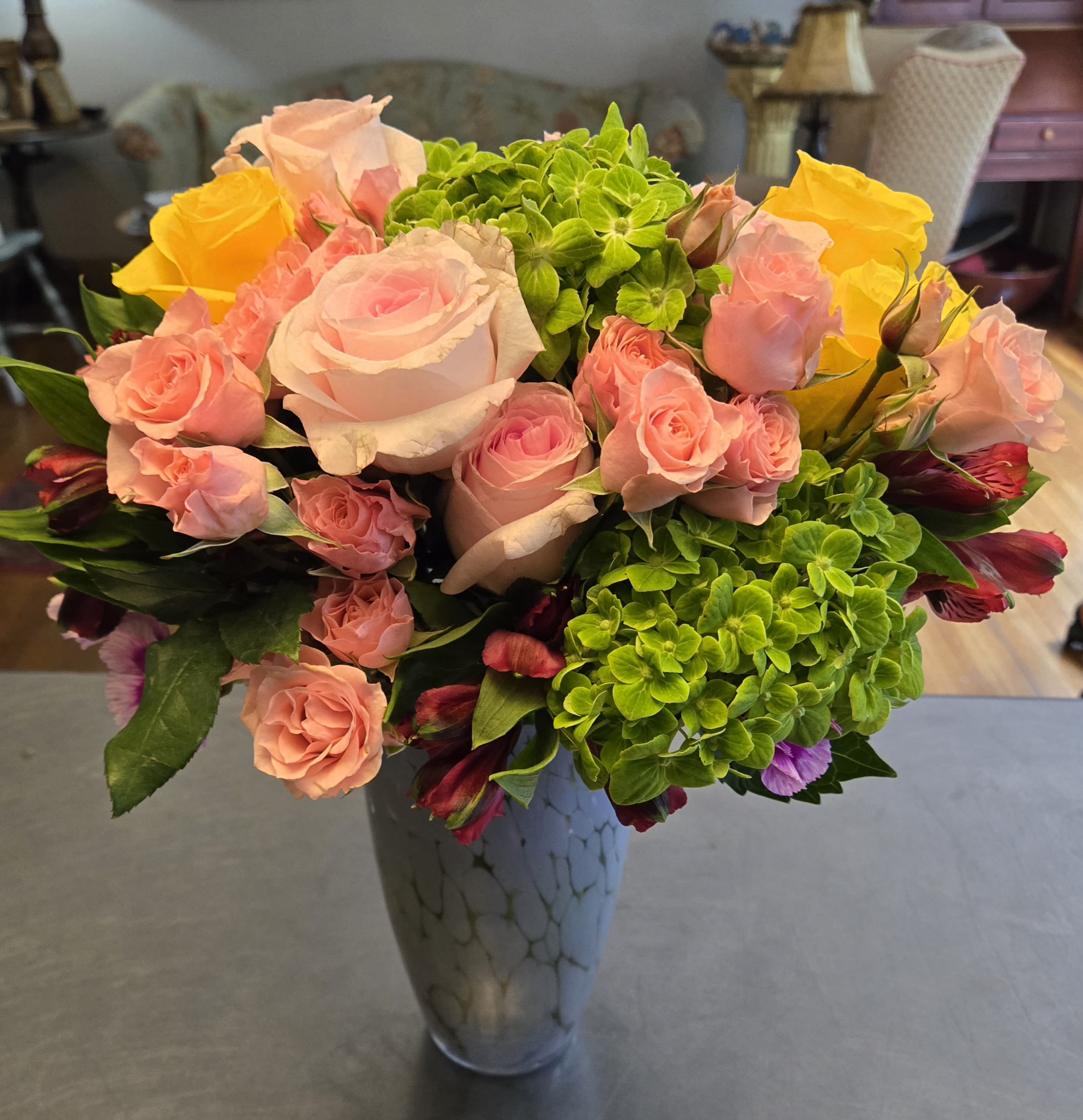 Pink and yellow roses with green hydrangeas in a tall vase