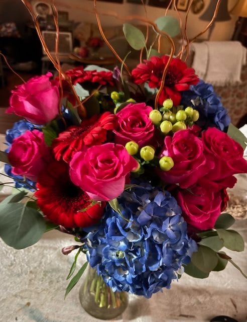 Bouquet of pink roses, red gerberas, and blue hydrangeas in a glass vase