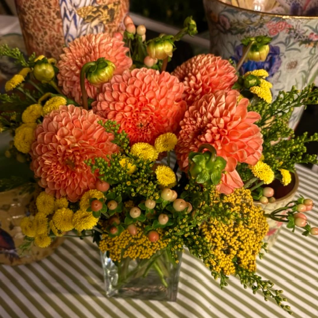 Coral dahlias and yellow filler flowers in a clear glass vase