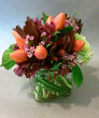 Orange tulips and pink flowers arranged in a glass vase