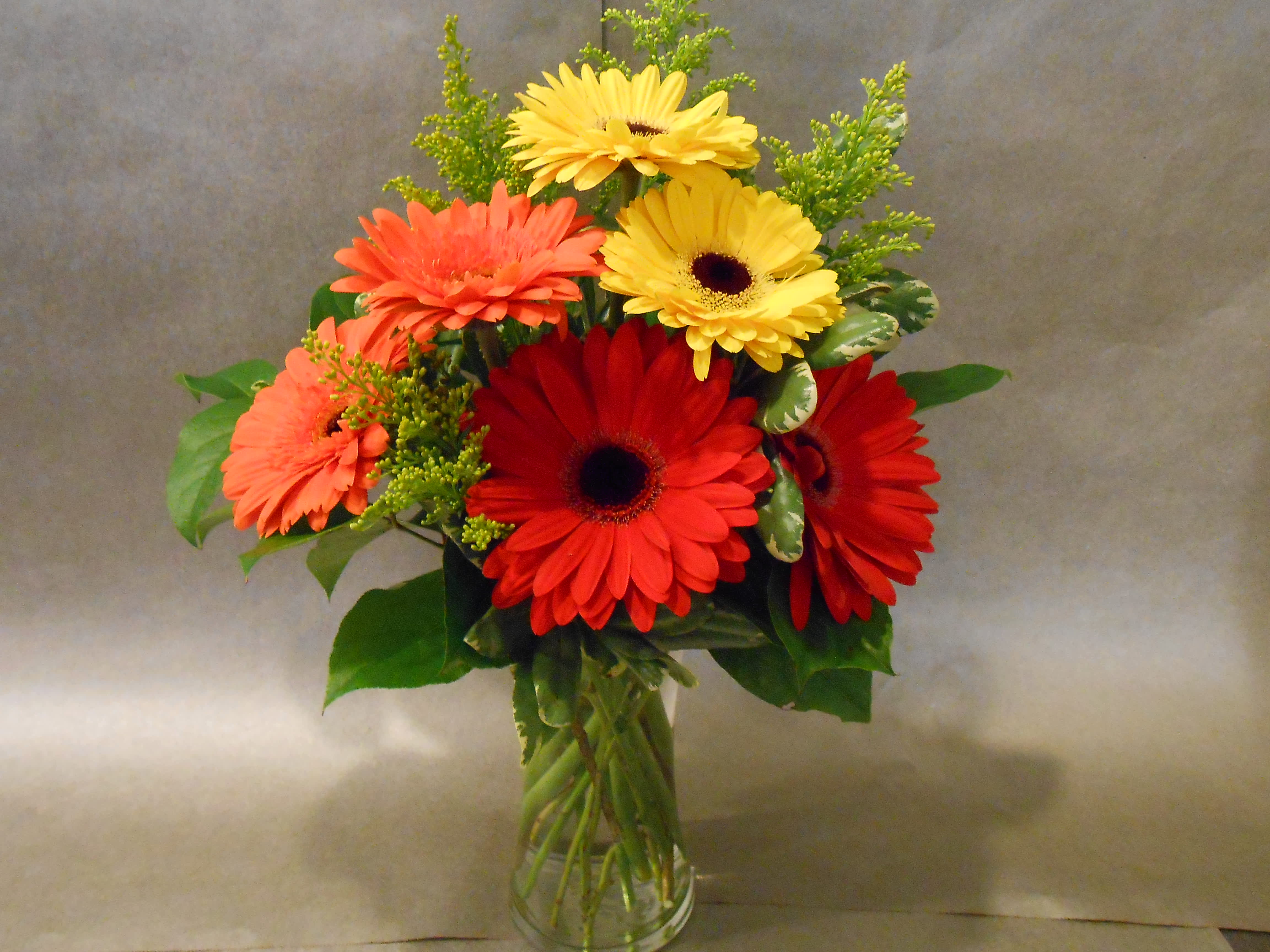 Bouquet of red, coral, and yellow gerbera daisies in a clear glass vase
