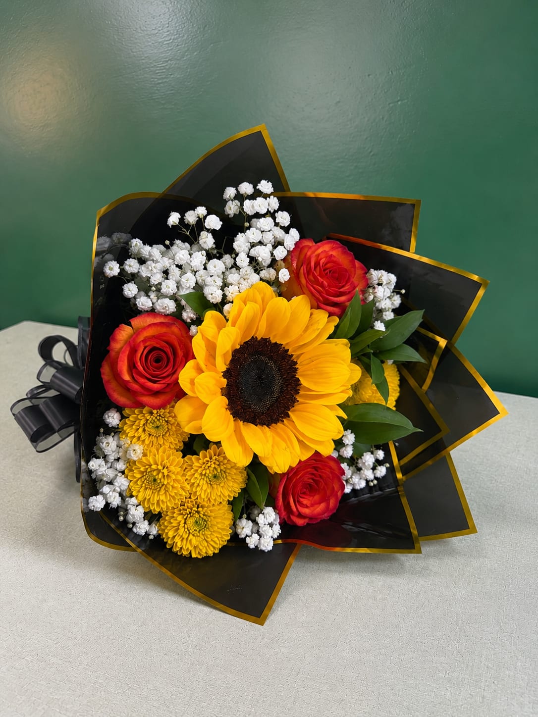 Bouquet of sunflowers, red roses, and white baby's breath in black wrap