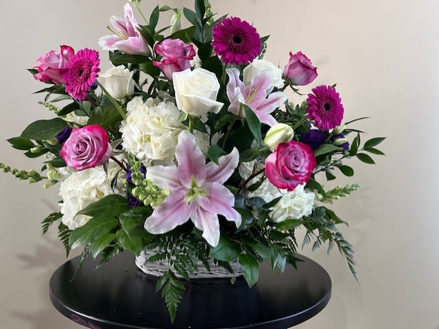 Basket arrangement of pink lilies, roses, gerbera daisies, and white hydrangeas in a white wicker container