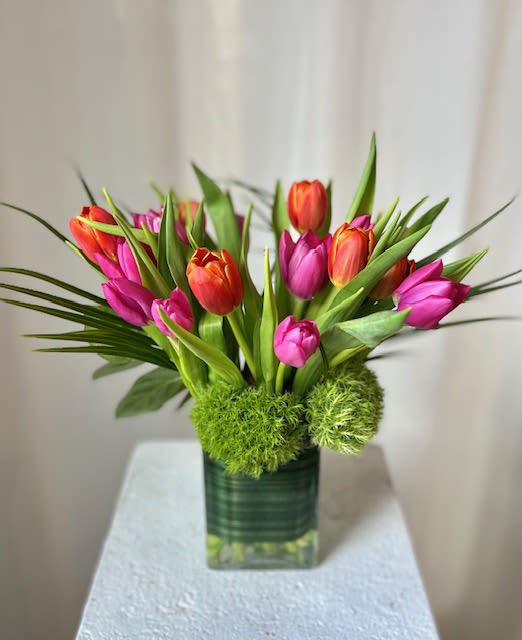 Pink and orange tulips arranged in a square glass vase with green accents
