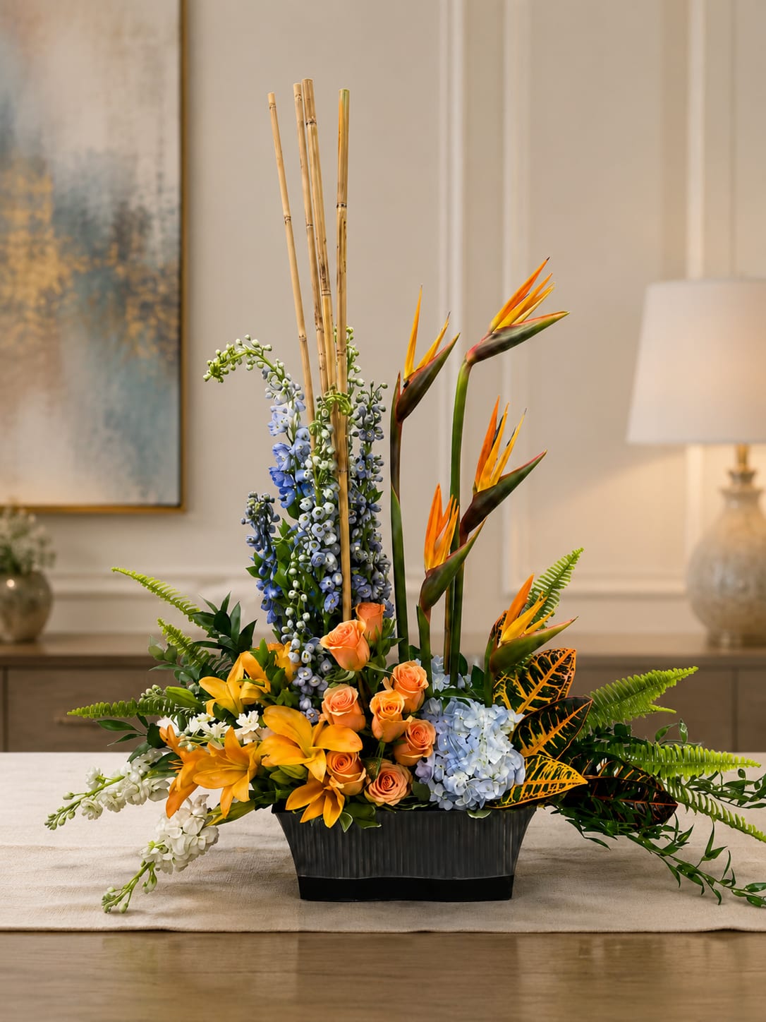 Tropical floral arrangement with orange birds of paradise, roses, lilies, and blue blooms in a black vase