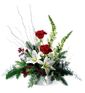 Low holiday arrangement with red roses, white lilies, and evergreens in a white container