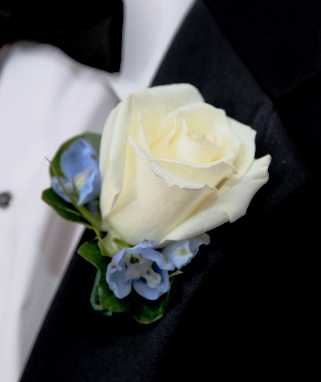 White rose boutonniere with small blue flowers on a black suit lapel