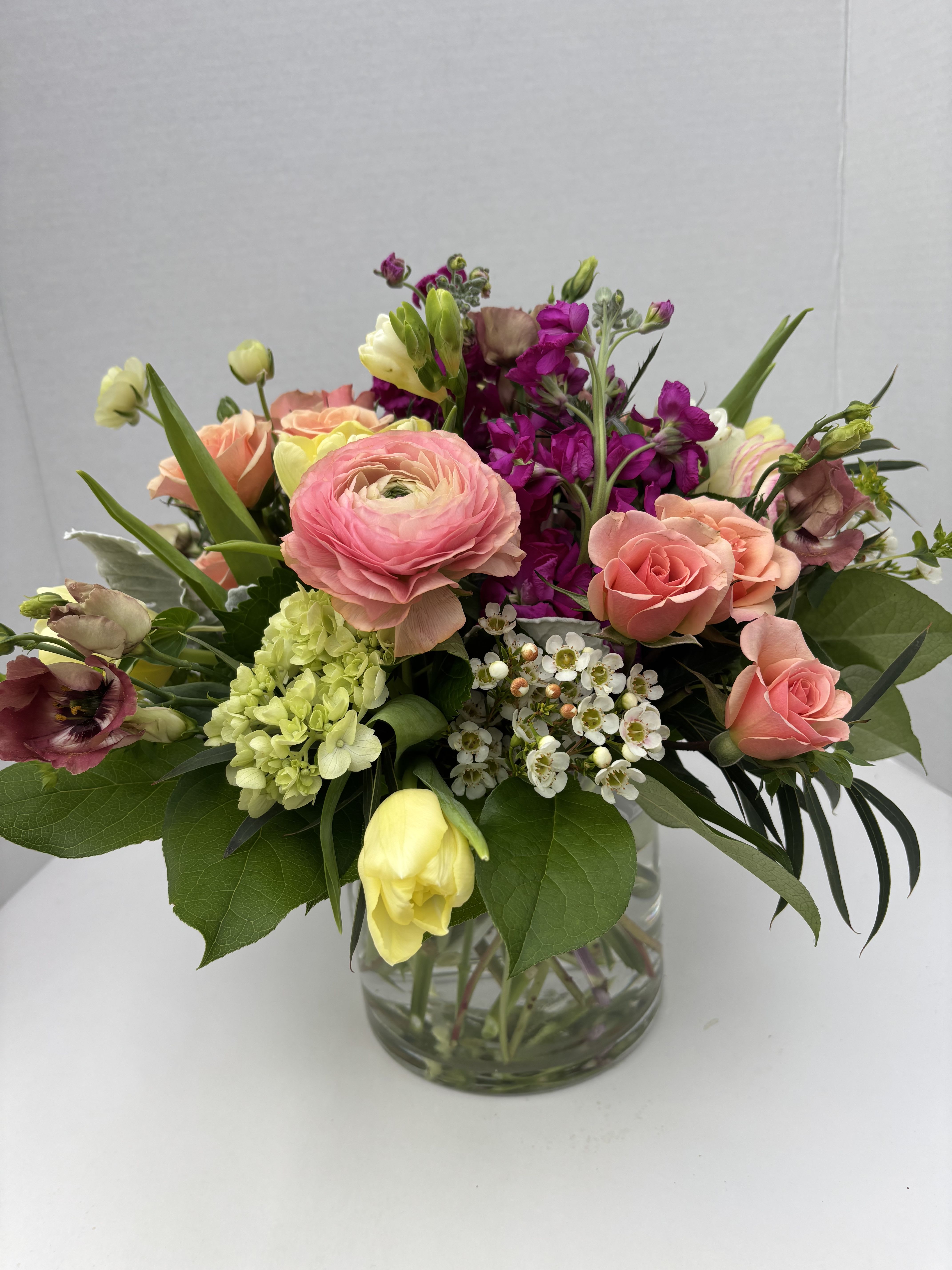 Mixed bouquet of pink, peach, yellow, and purple flowers in a glass vase