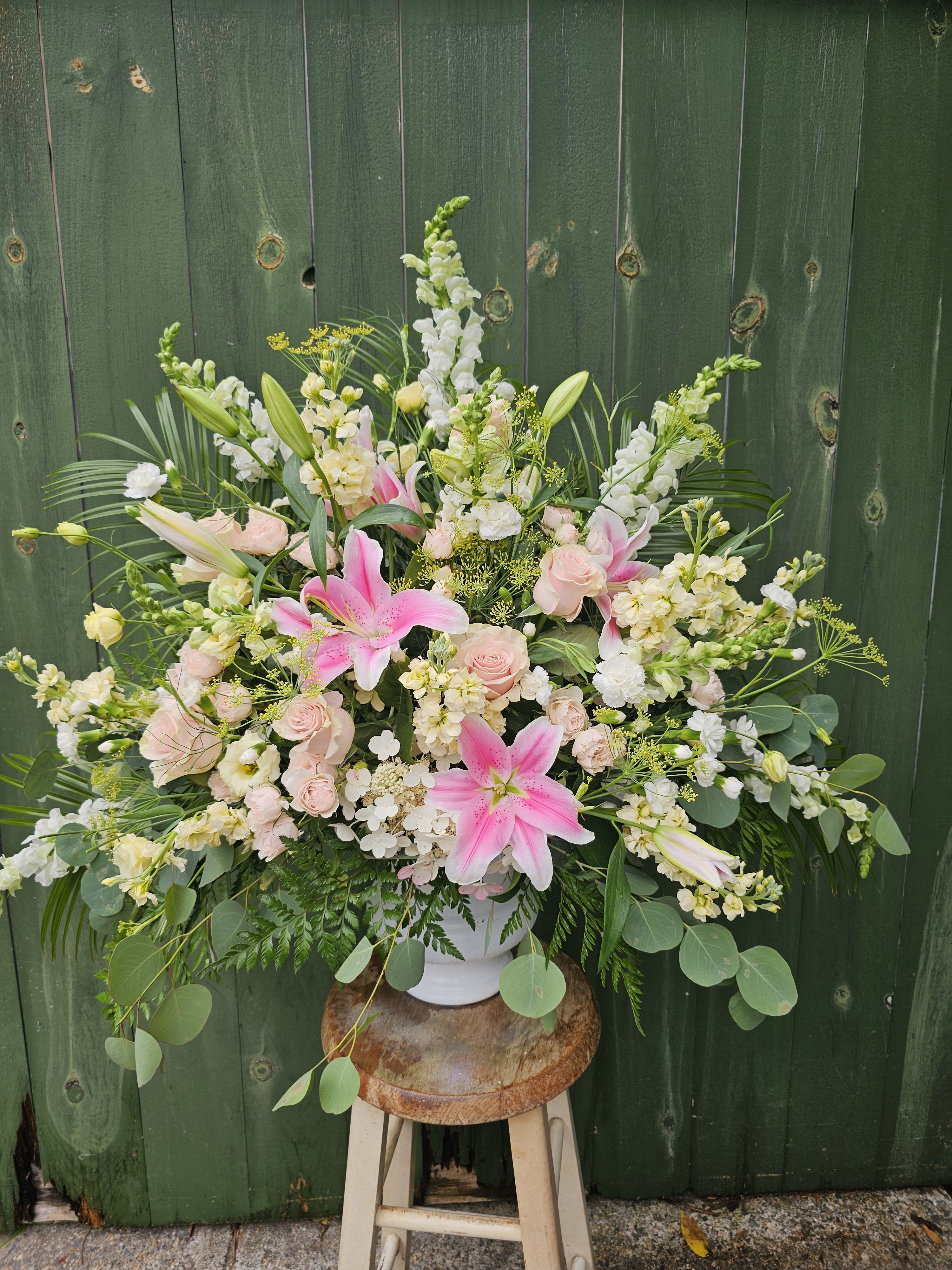 Large pastel floral arrangement in a white vase with pink lilies and roses