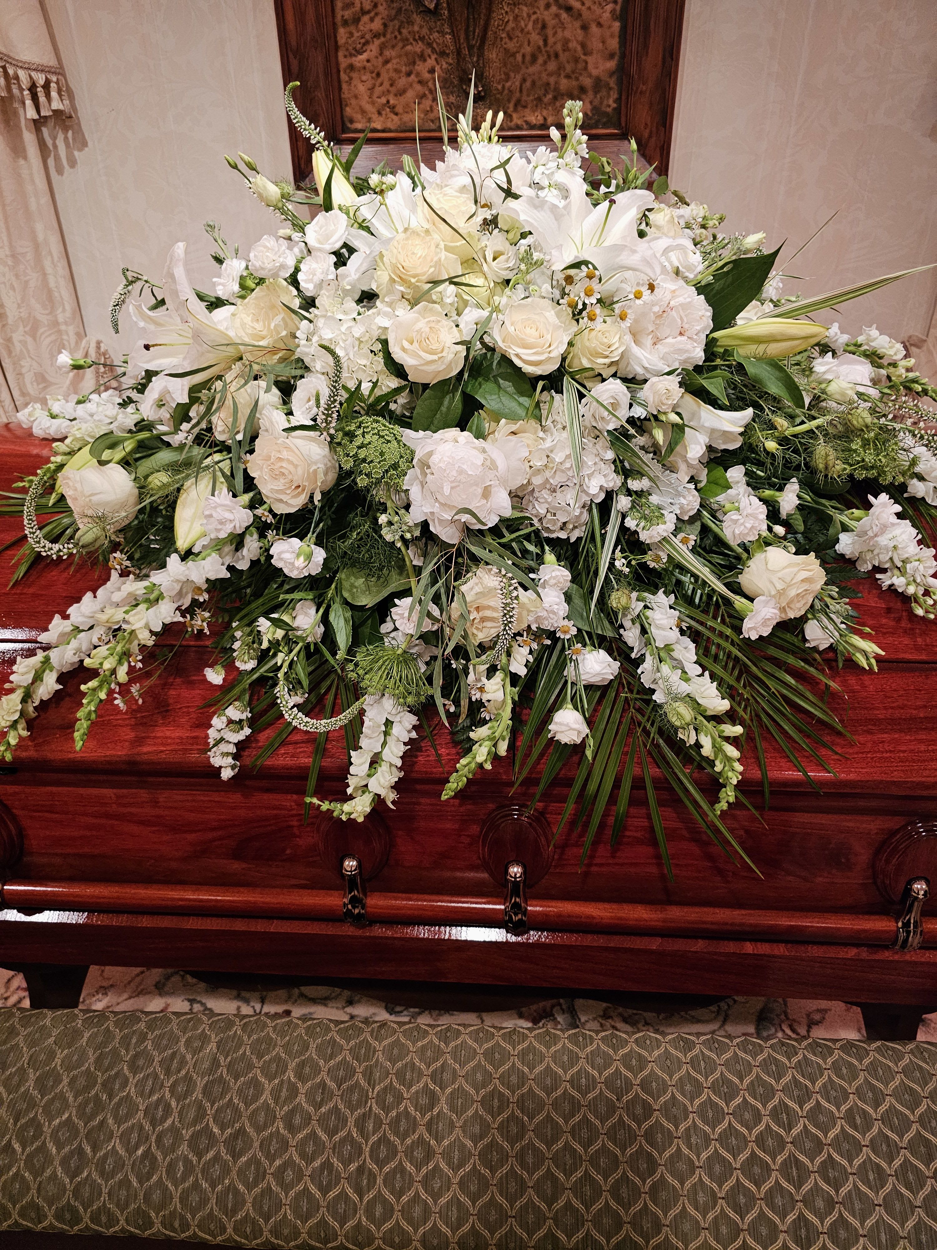 Large white floral spray on a polished wooden casket