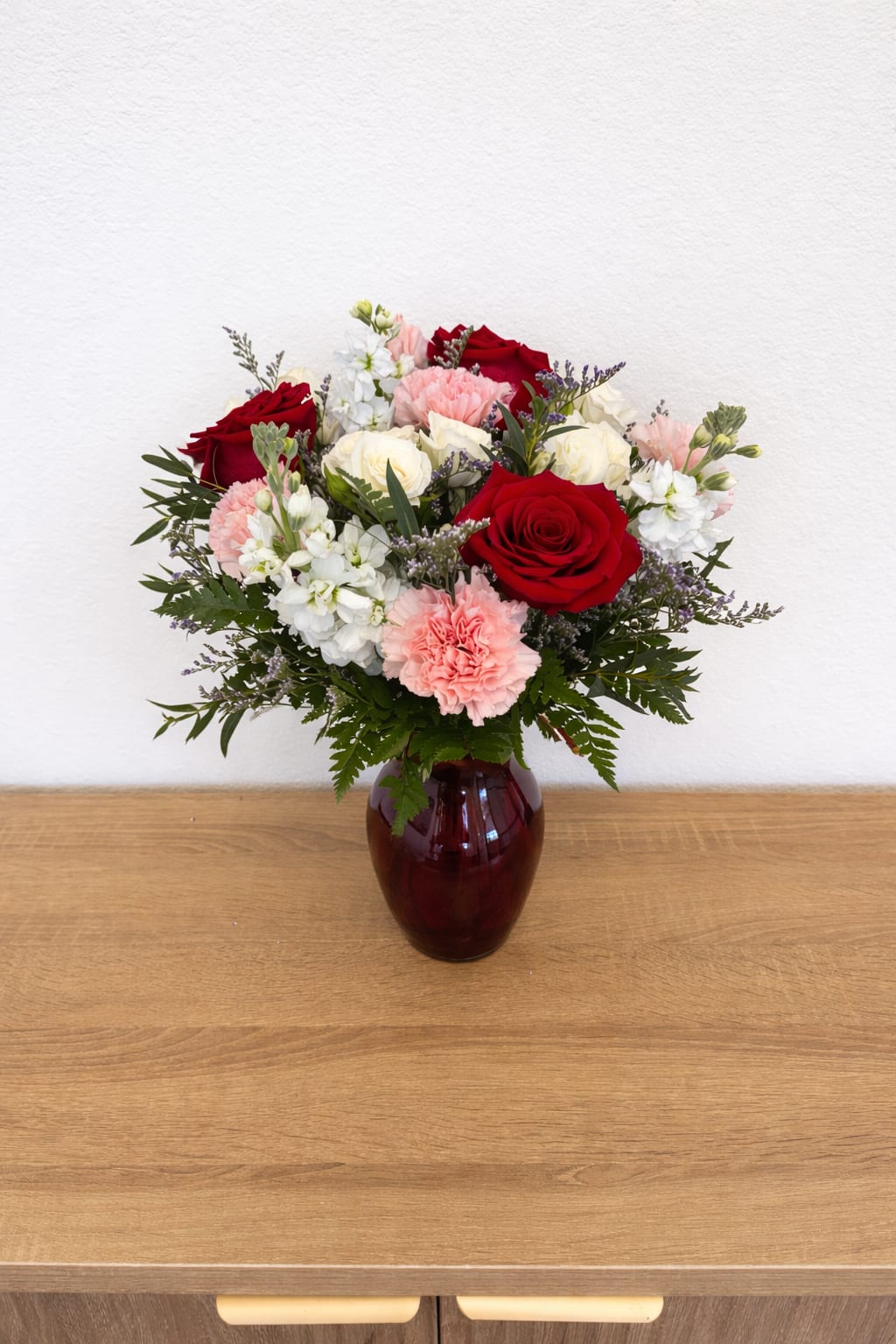 Bouquet of red and white roses with pink carnations in a burgundy vase