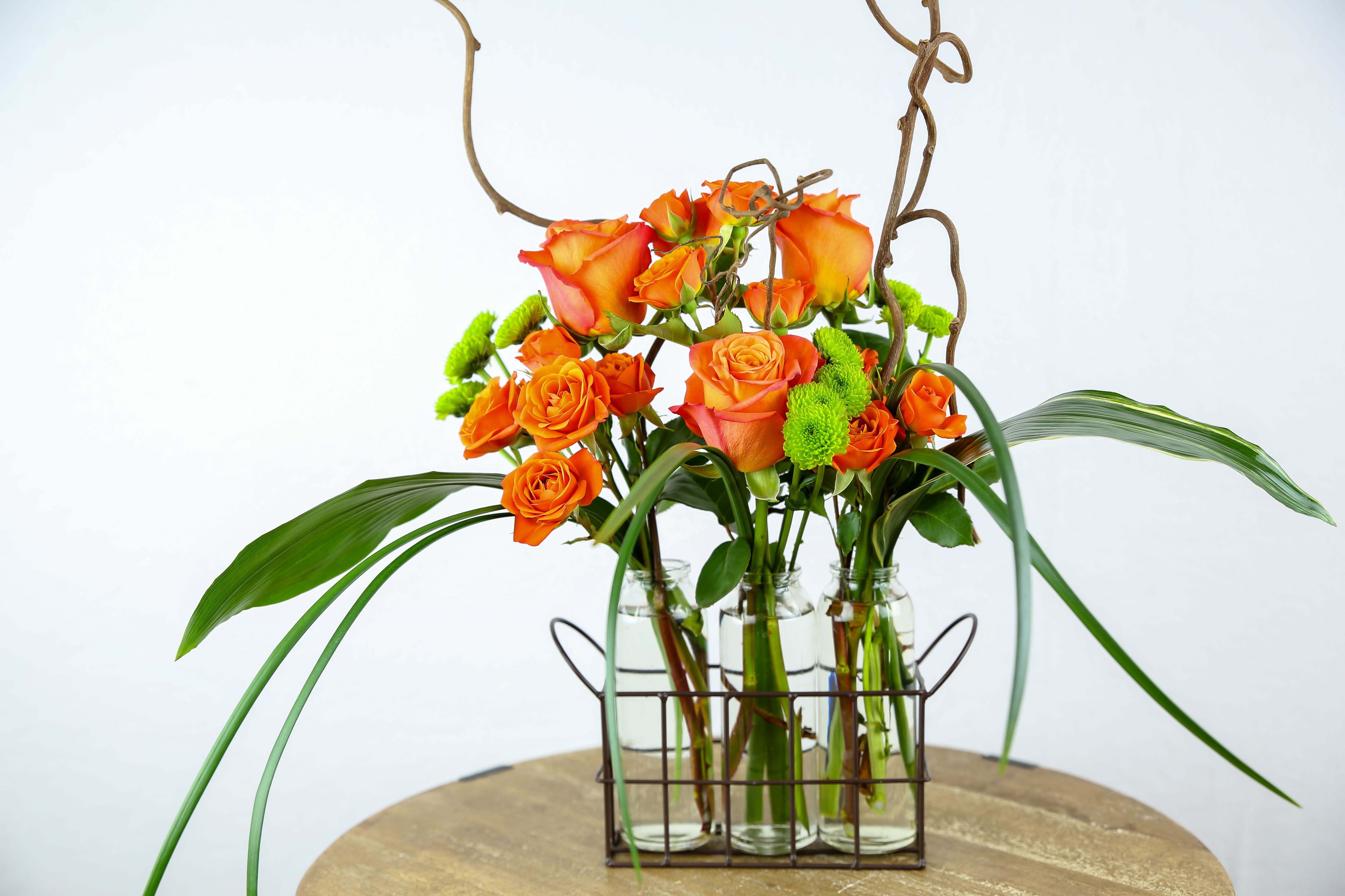 Orange roses in glass bottles with curly branches and green accents